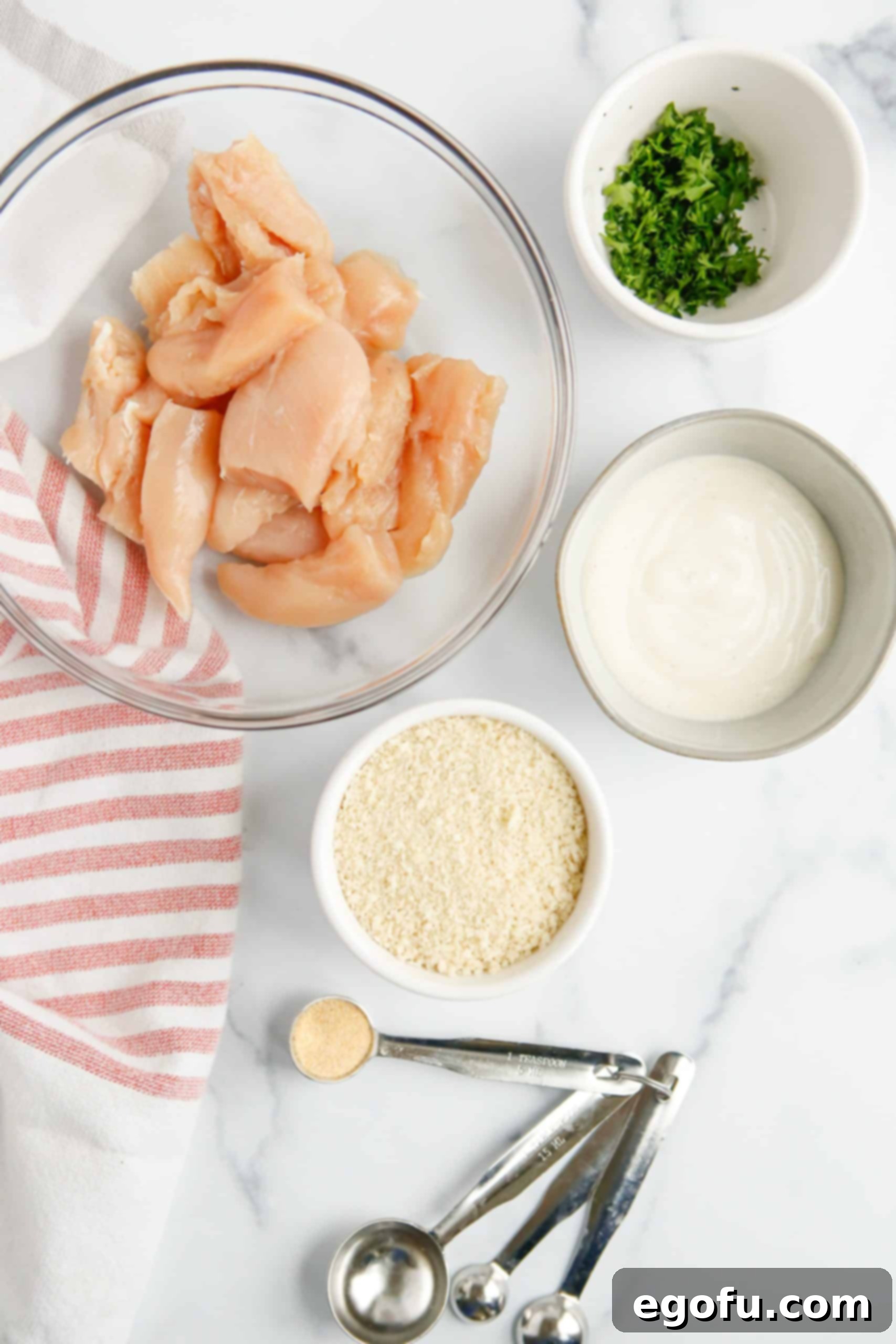 Ingredients for Easy Baked Ranch Chicken Nuggets: diced chicken breasts, Panko breadcrumbs, ranch dressing, parsley, and garlic powder laid out.