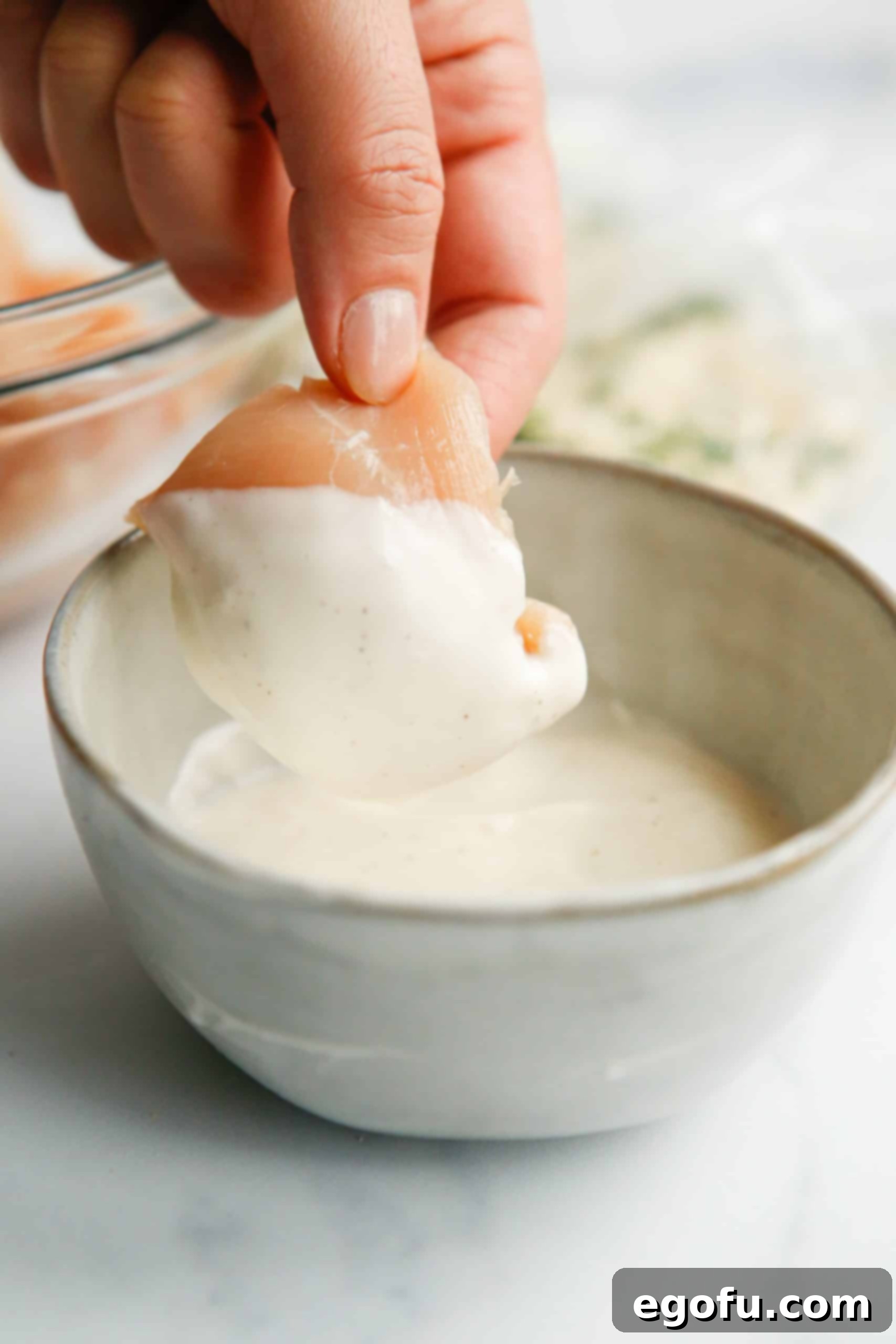 Hand dipping piece of chicken into ranch dressing in a bowl, showing full coating.
