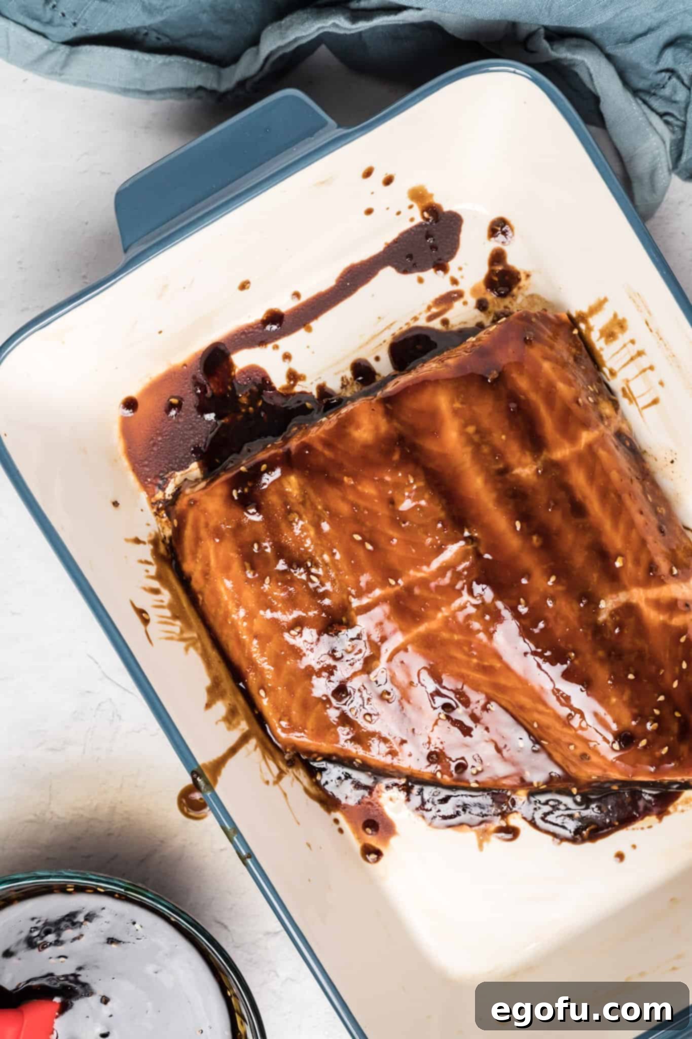 A perfectly glazed cut of salmon resting in a baking dish, its surface glistening with teriyaki sauce, just before or after baking.