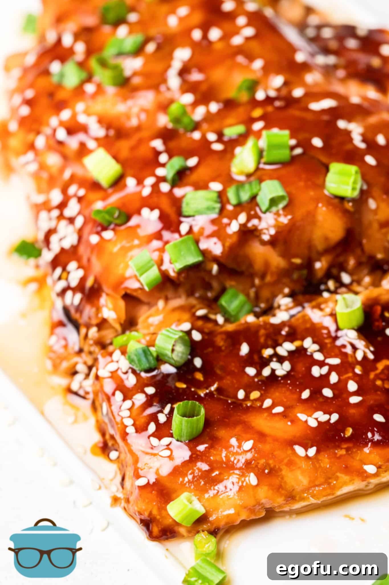 A close-up view of a baked salmon fillet, beautifully glazed with teriyaki sauce and topped with an abundance of white sesame seeds and vibrant chopped green onions, ready to be enjoyed.