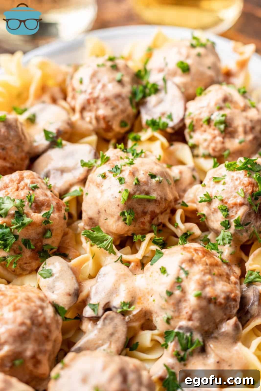 Closeup photo of Crock Pot Meatball Stroganoff served over egg noodles on a white plate, garnished with fresh parsley.