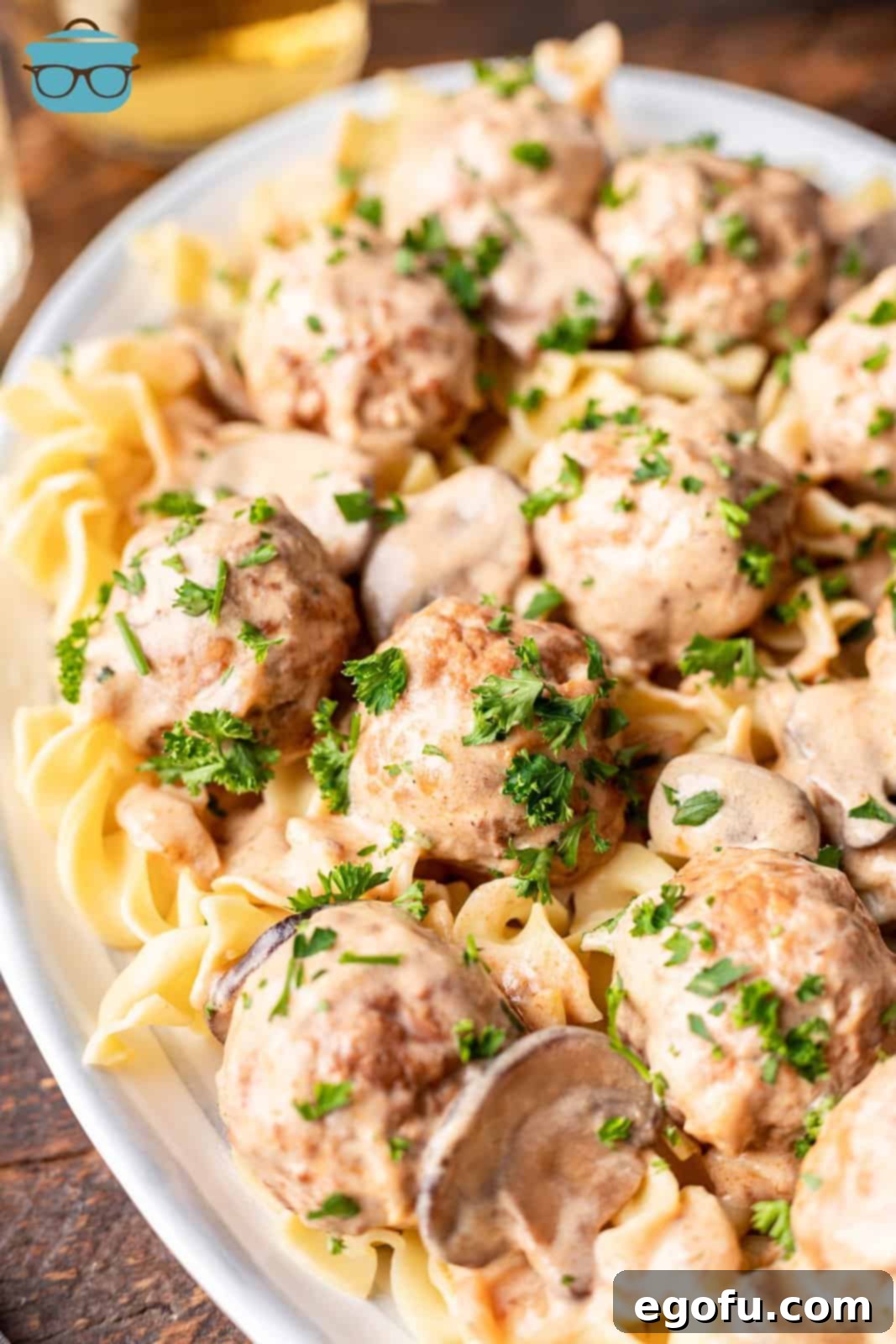 Meatball stroganoff served over egg noodles on a long oval white plate, showcasing the creamy sauce.