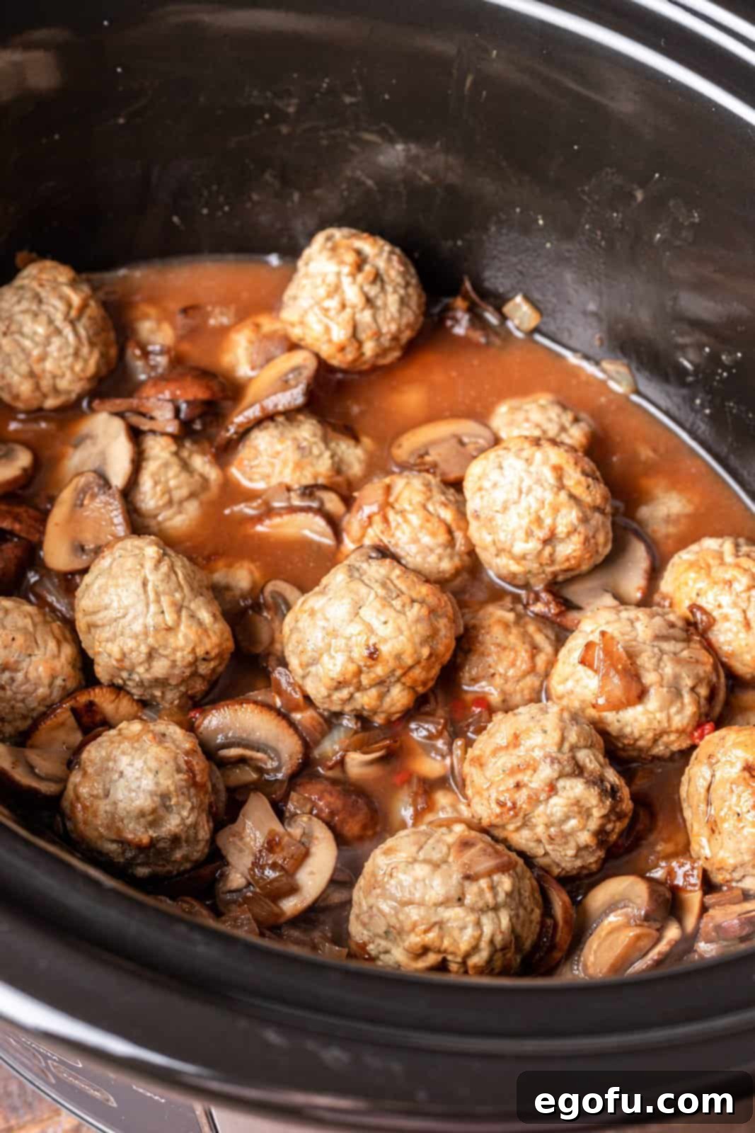 Beef broth mixture poured over meatballs in an oval slow cooker before cooking.