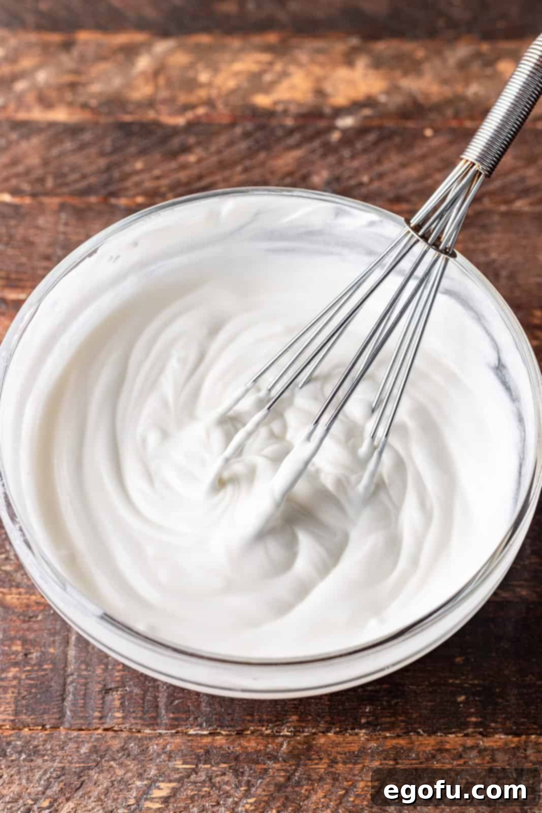 Water, cornstarch, and sour cream being whisked together in a clear bowl to create a smooth mixture.