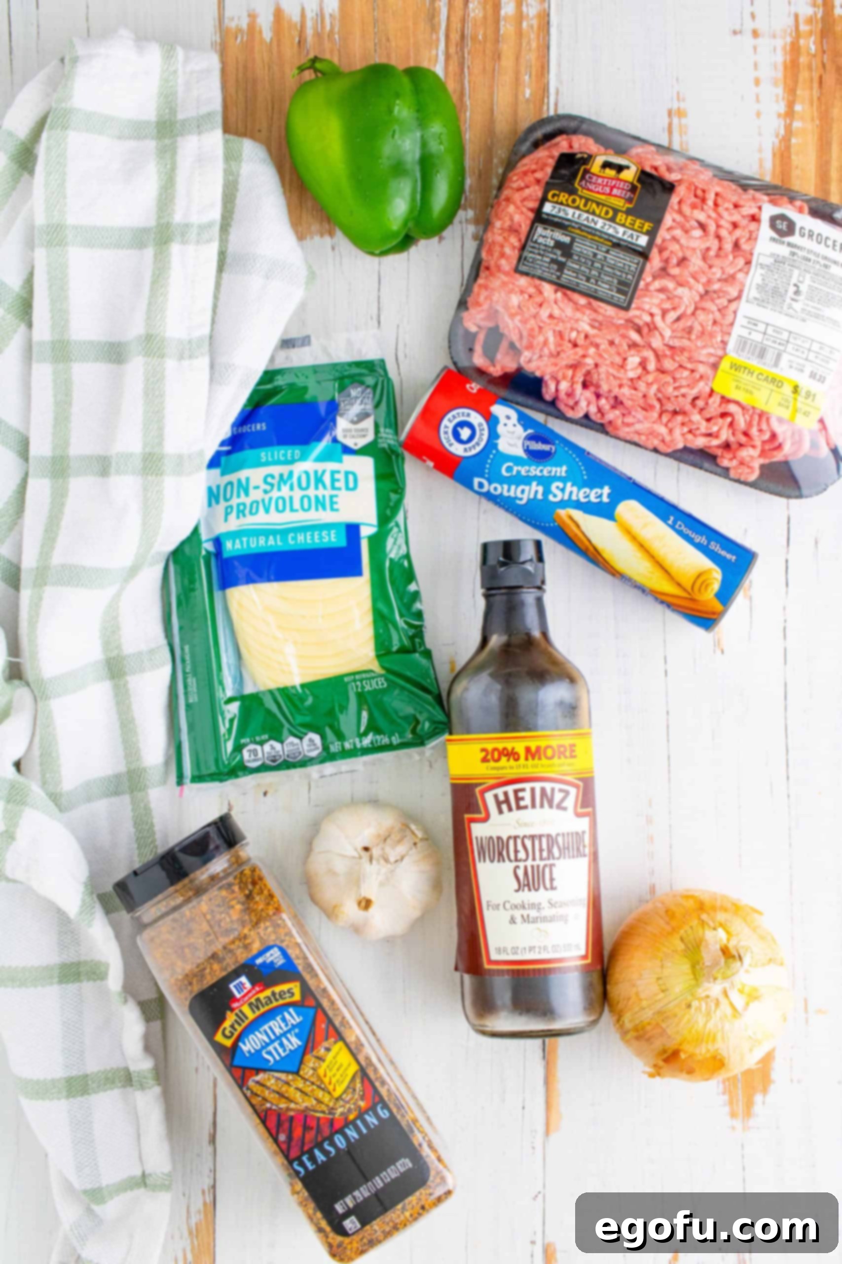 Philly Cheesesteak Poppers 4 Ingredients for Philly Cheesesteak Cups laid out: butter, onion, green bell pepper, garlic, lean ground beef, Worcestershire sauce, steak seasoning, crescent roll dough sheet, provolone cheese.