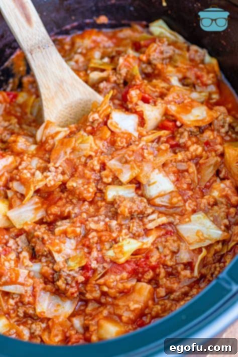 a wooden spoon inserted cooked unstuffed cabbage rolls in a slow cooker.