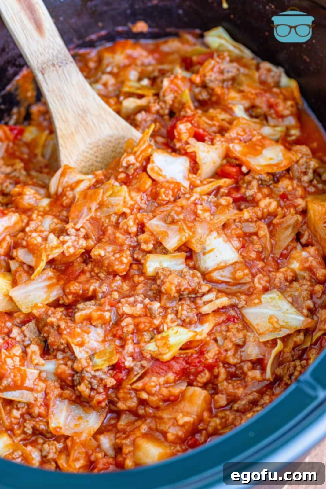 A wooden spoon inserted into a slow cooker filled with perfectly cooked unstuffed cabbage rolls, ready to be served.