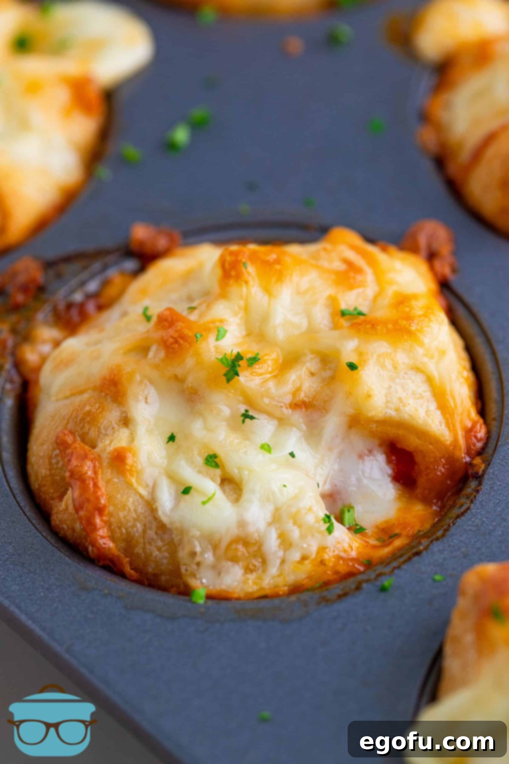 A perfectly baked chicken parmesan cup sitting in a muffin tin, golden brown and bubbly.