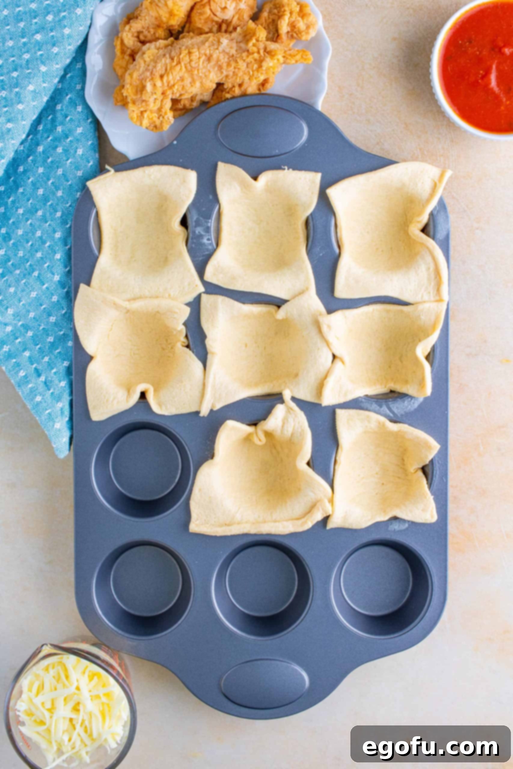 Crescent roll dough pieces cut and pressed into a muffin tin, forming cups for the chicken parmesan filling.