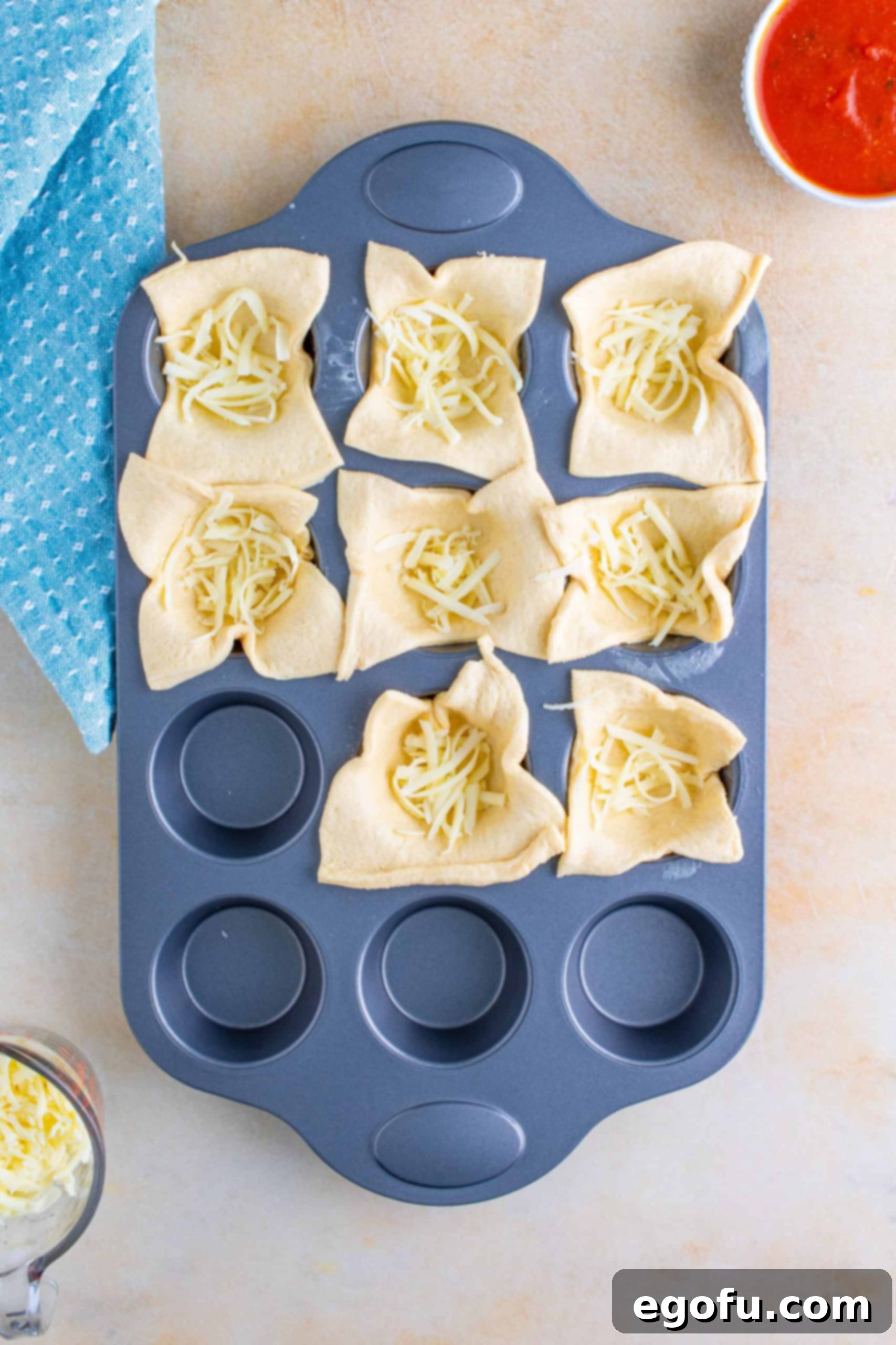 The first layer of shredded mozzarella cheese evenly distributed into the crescent dough cups in a muffin tin.