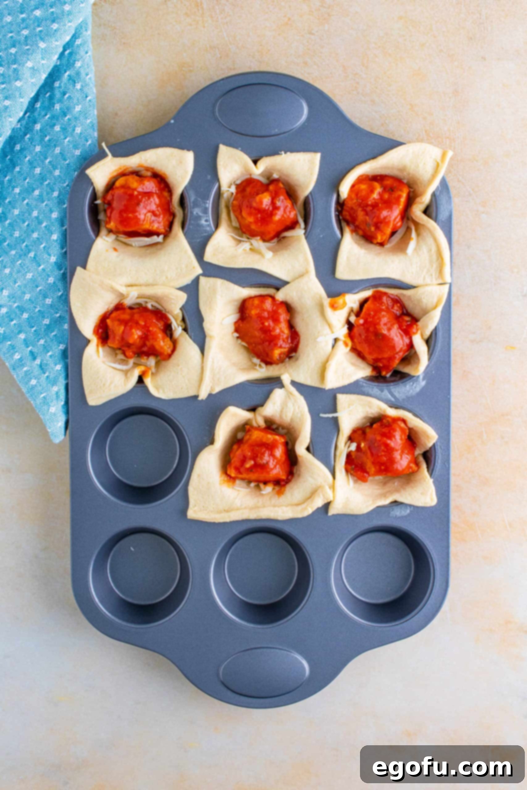 Pieces of chicken dipped in marinara sauce placed on top of the cheese layer in the crescent dough cups.