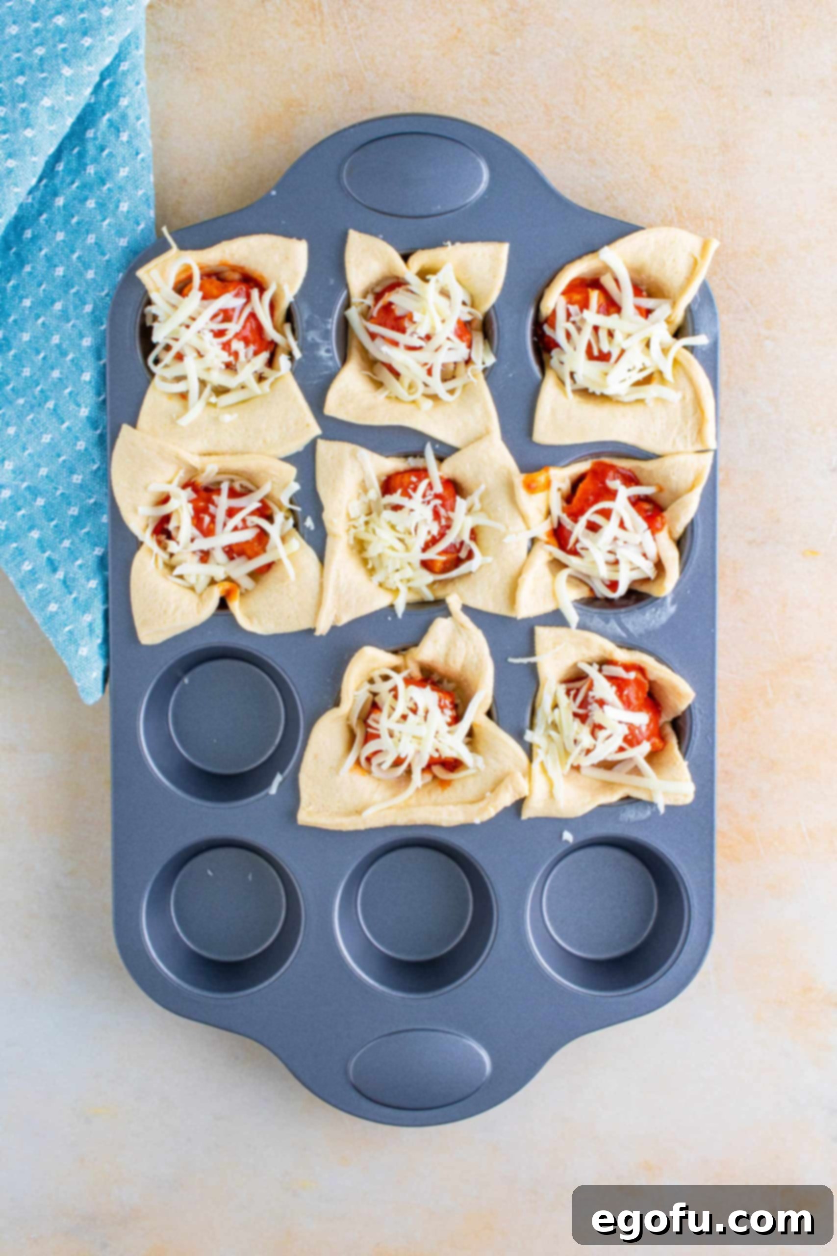 A second layer of mozzarella cheese being added on top of the chicken and marinara sauce filling in the muffin tin cups.