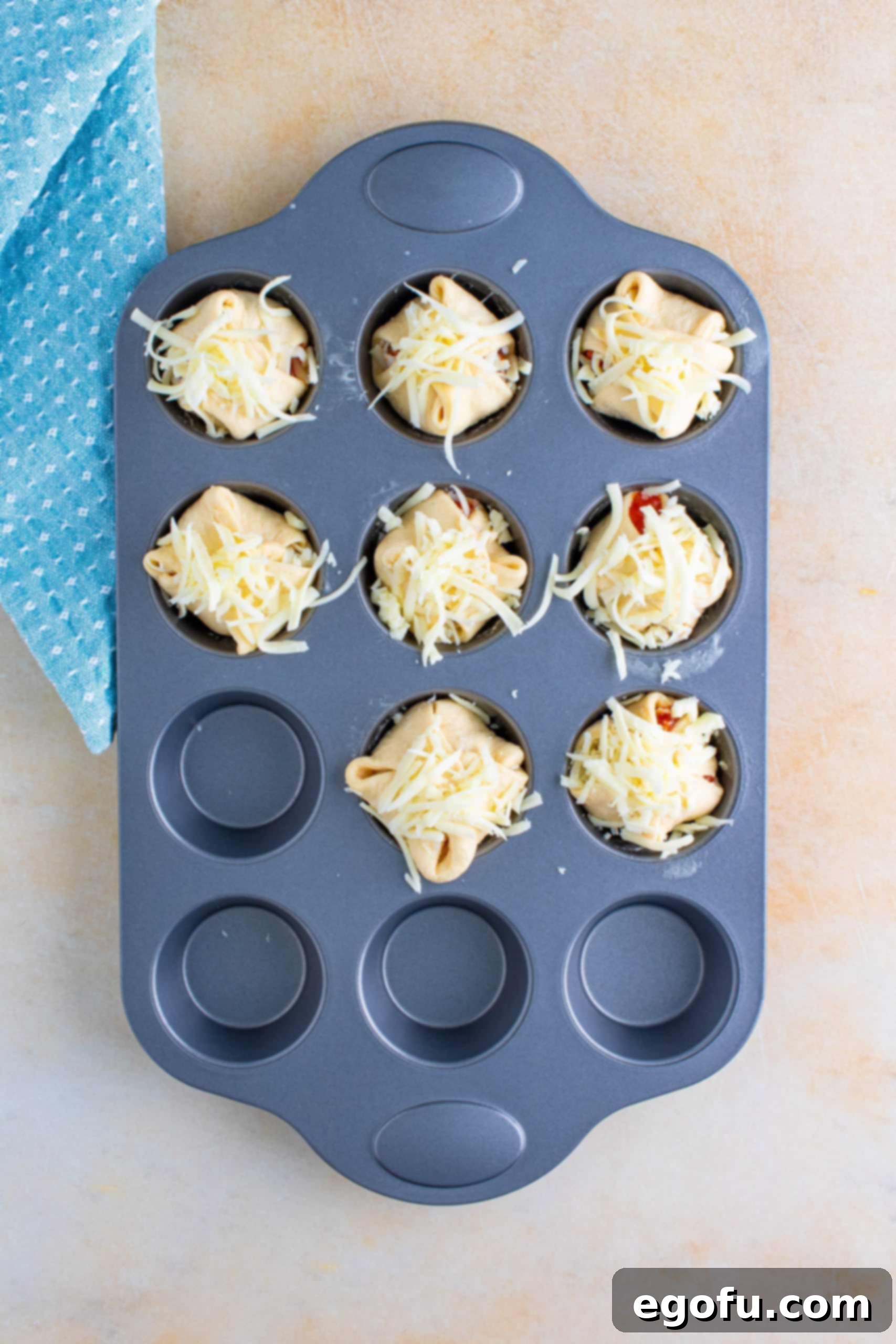 The assembled chicken parmesan cups in the muffin tin, topped with additional cheese before baking.