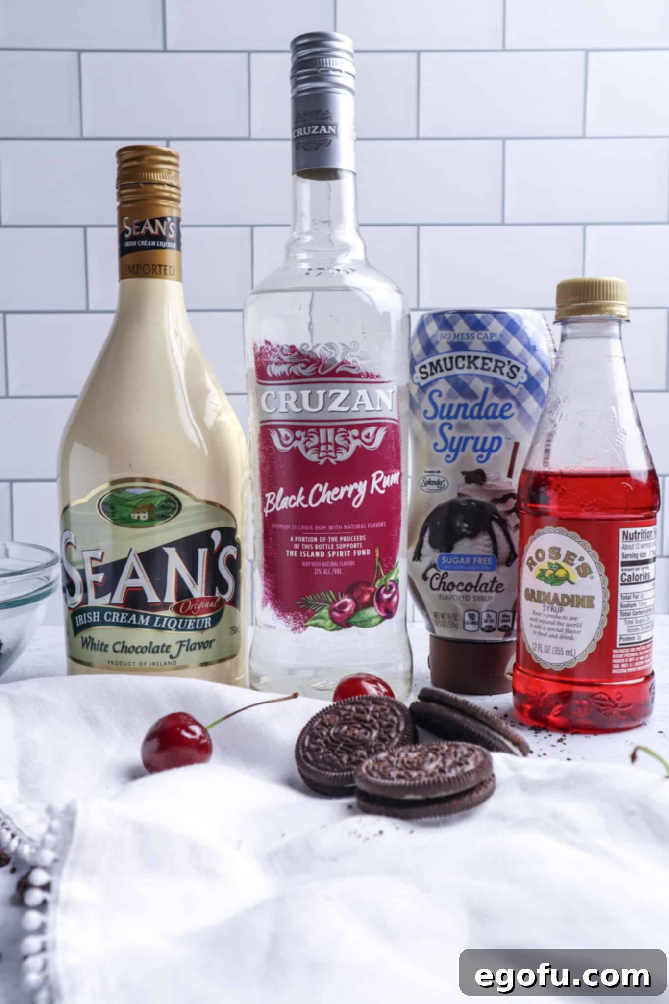 A visual display of the ingredients needed to make a Cherry Garcia Martini: White Chocolate Irish cream, Black Cherry Rum, Grenadine, and Chocolate Syrup, arranged for clarity.