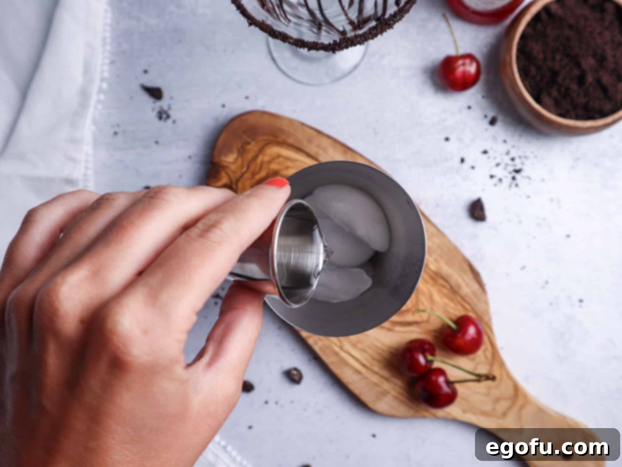 Cherry rum being poured over ice in a cocktail shaker, illustrating the first liquid ingredient addition.