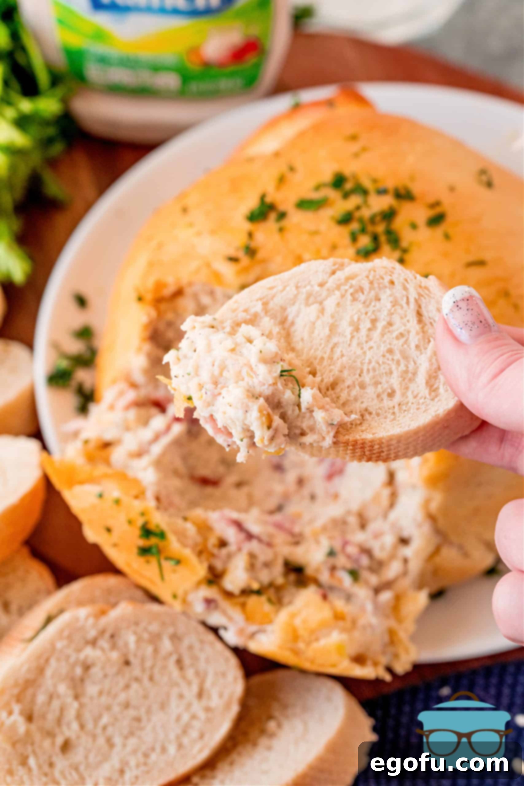 A hand scooping a generous portion of the creamy, cheesy chicken and bacon mixture out of a freshly baked Crack Chicken Ball, served alongside toasted bread slices.
