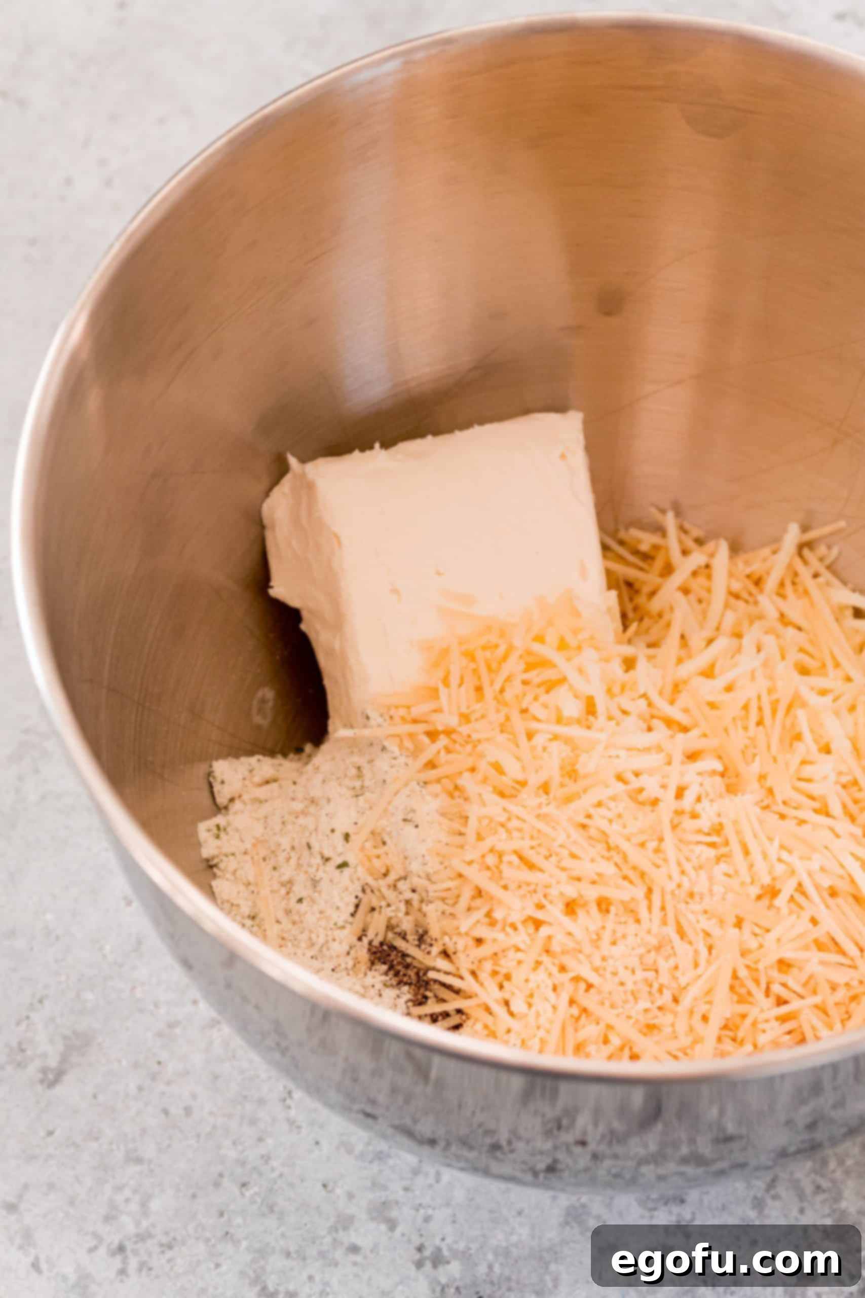 Softened cream cheese, shredded cheeses, and ranch seasoning ready to be mixed in a stand mixer bowl, forming the creamy base of the Crack Chicken Ball filling.