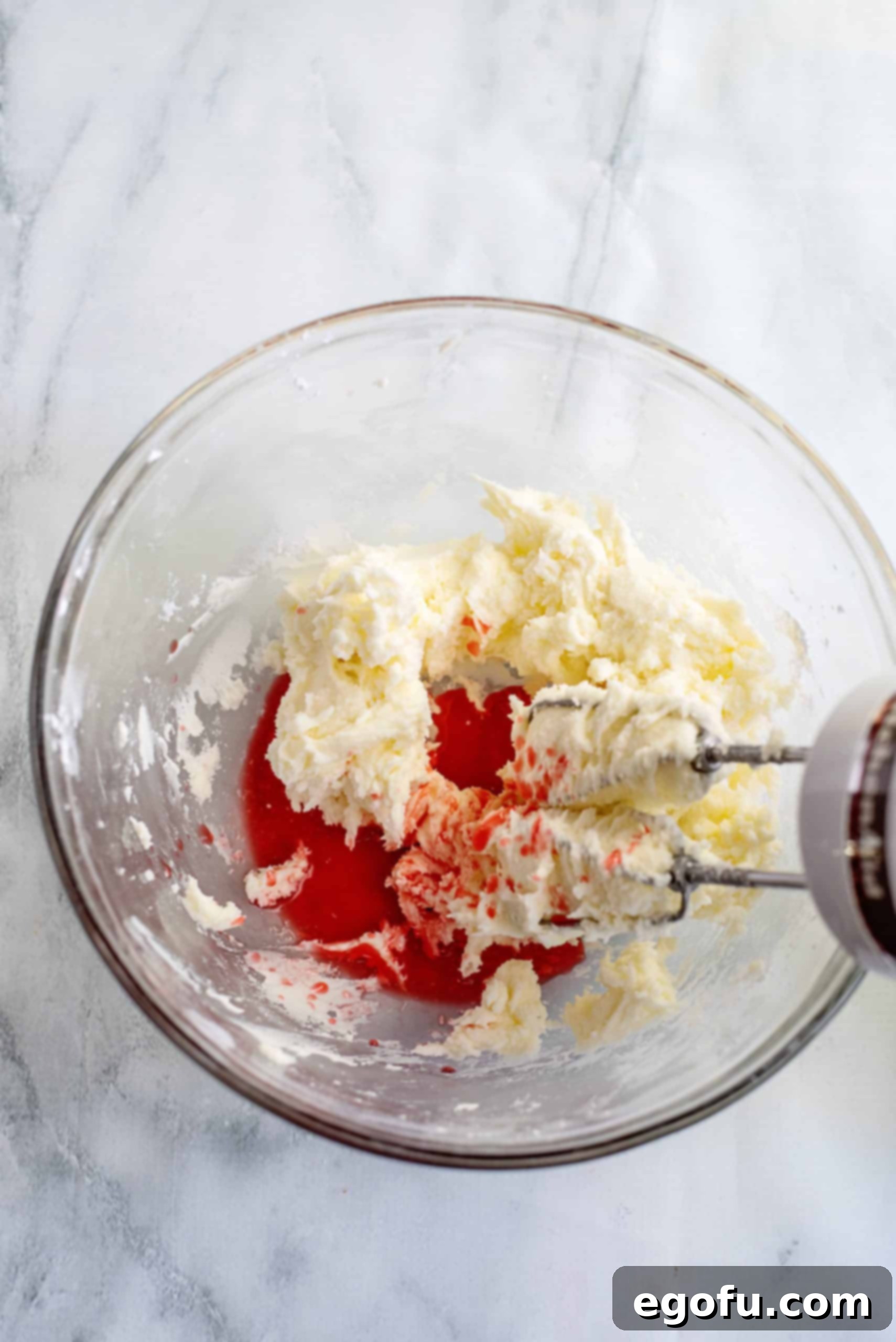 Blended butter and powdered sugar with maraschino cherry juice added in a bowl.