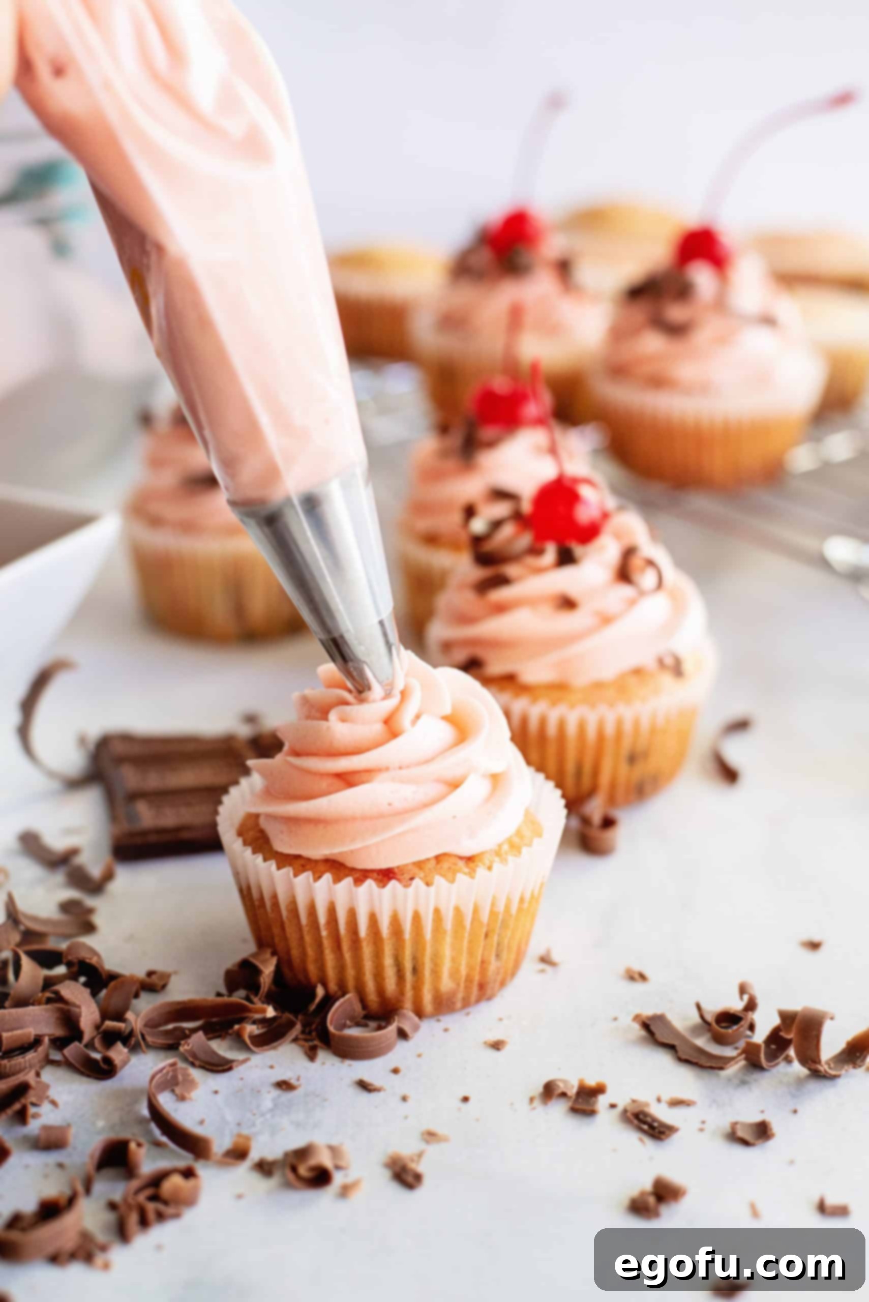 Cherry buttercream frosting being piped onto freshly baked Cherry Chocolate Chip Cupcakes.