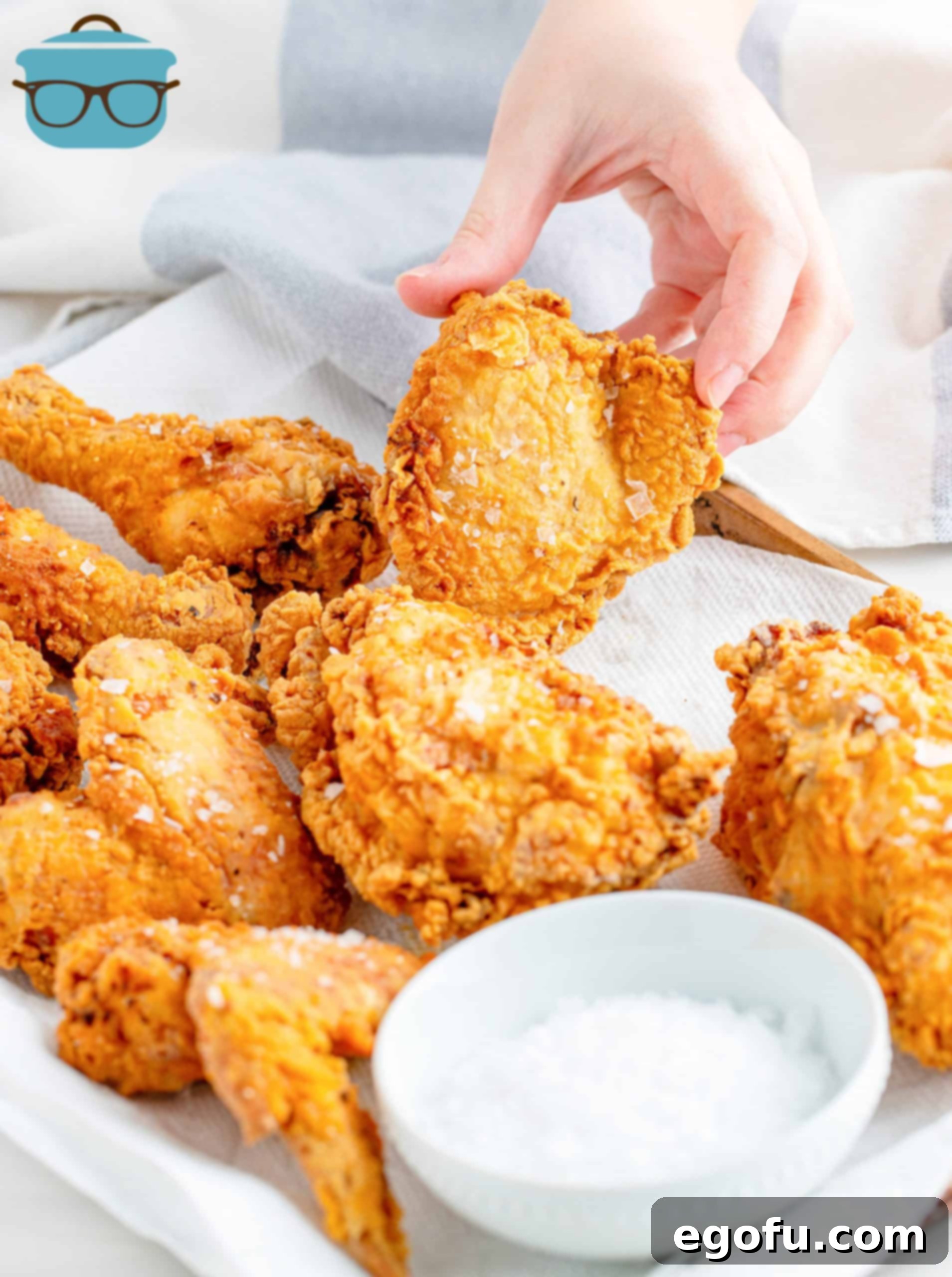 Chicken on paper towels with salt and hand holding up piece of Souther Fried Chicken.