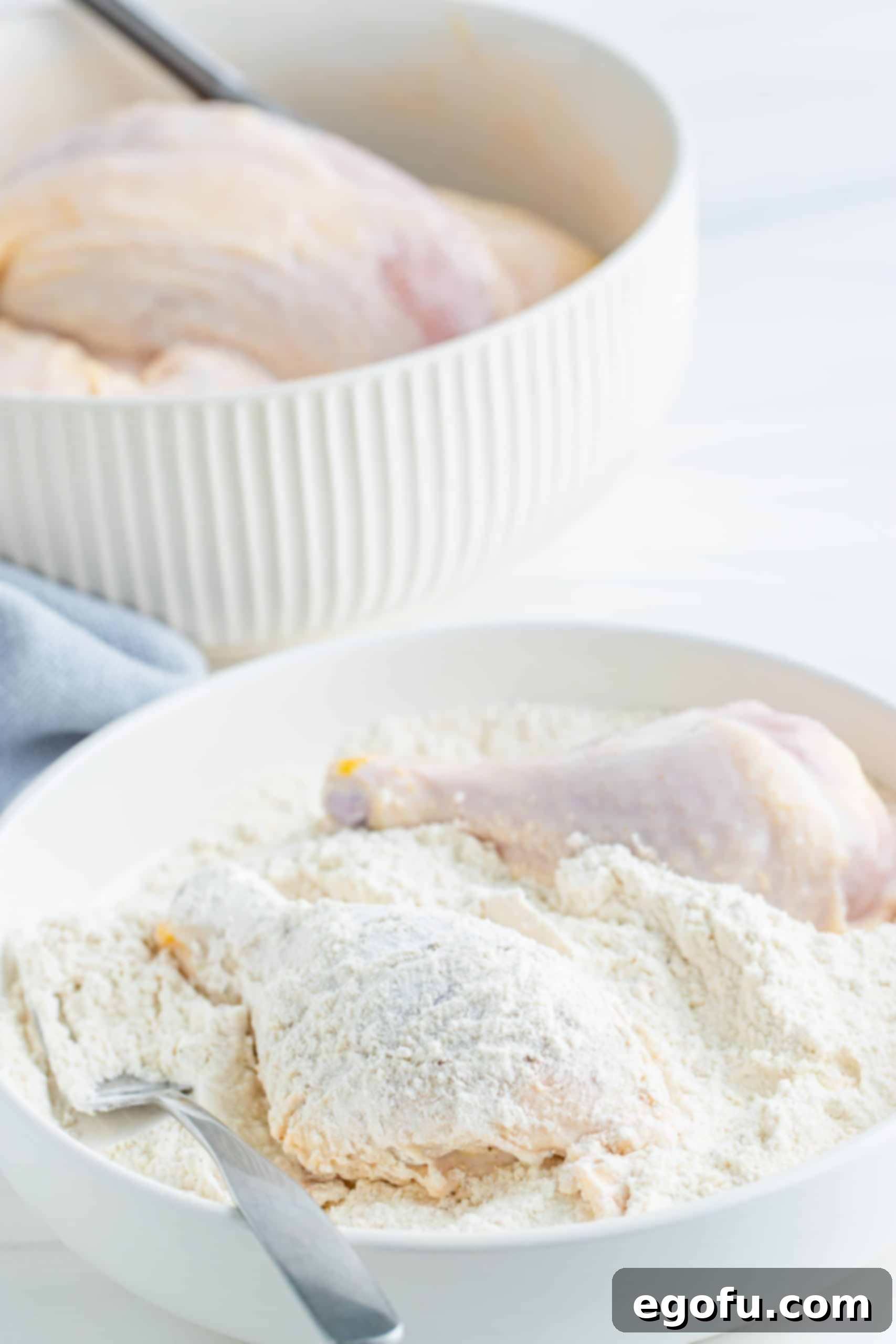 Chicken pieces being coated in flour mixture in white bowl with a fork. 