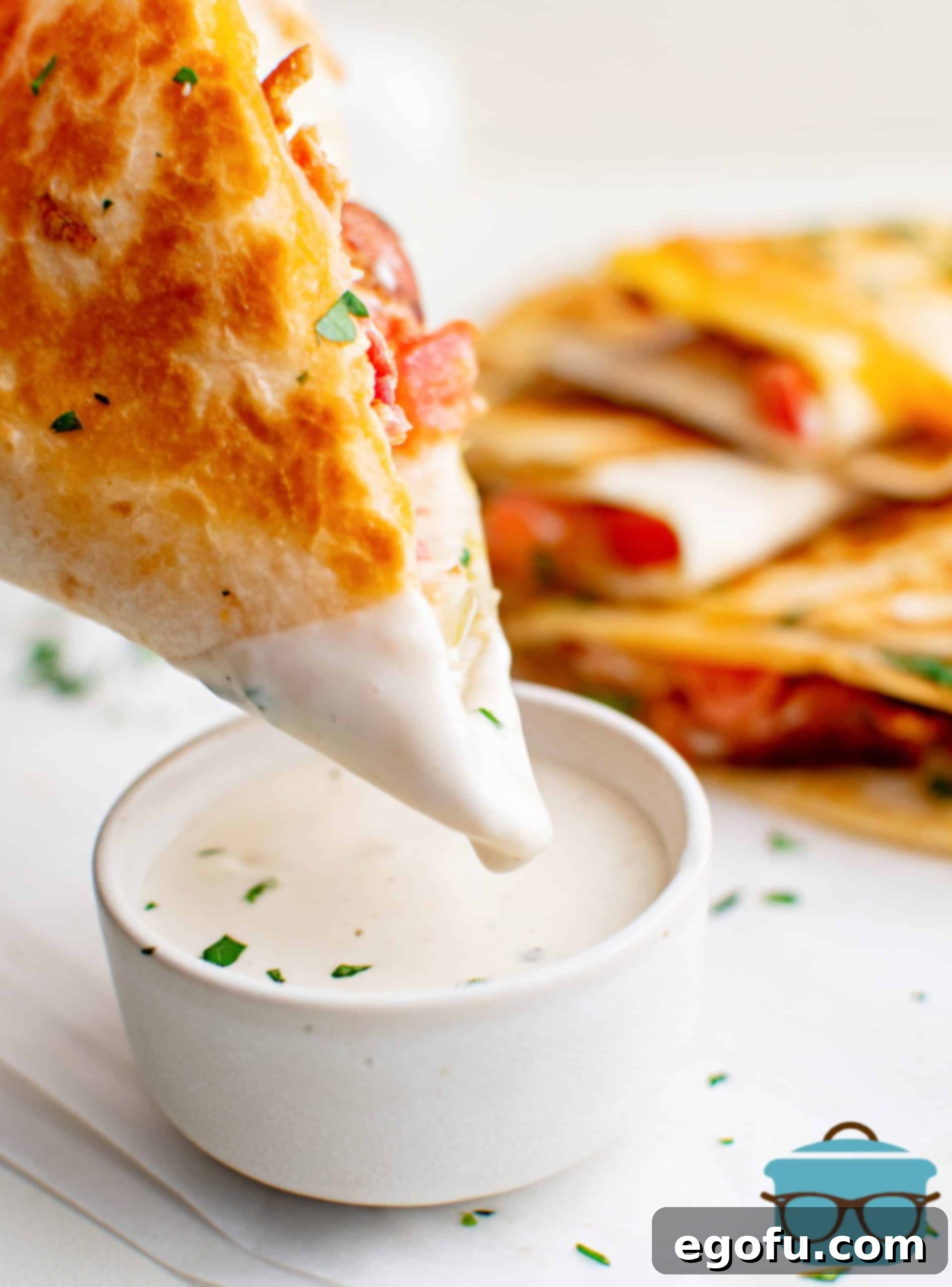 Hand dipping a golden BLT Quesadilla into a bowl of creamy dipping sauce.