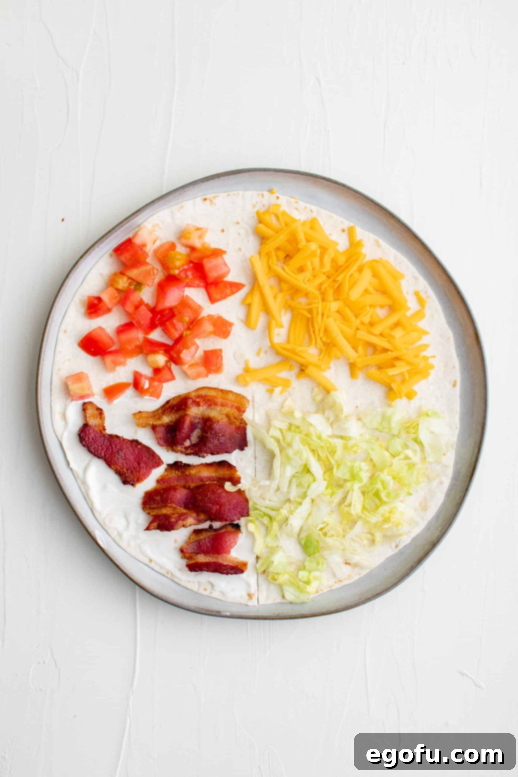 Bacon, tomatoes, cheese, and lettuce placed on separate four sections of a flour tortilla, ready for folding.