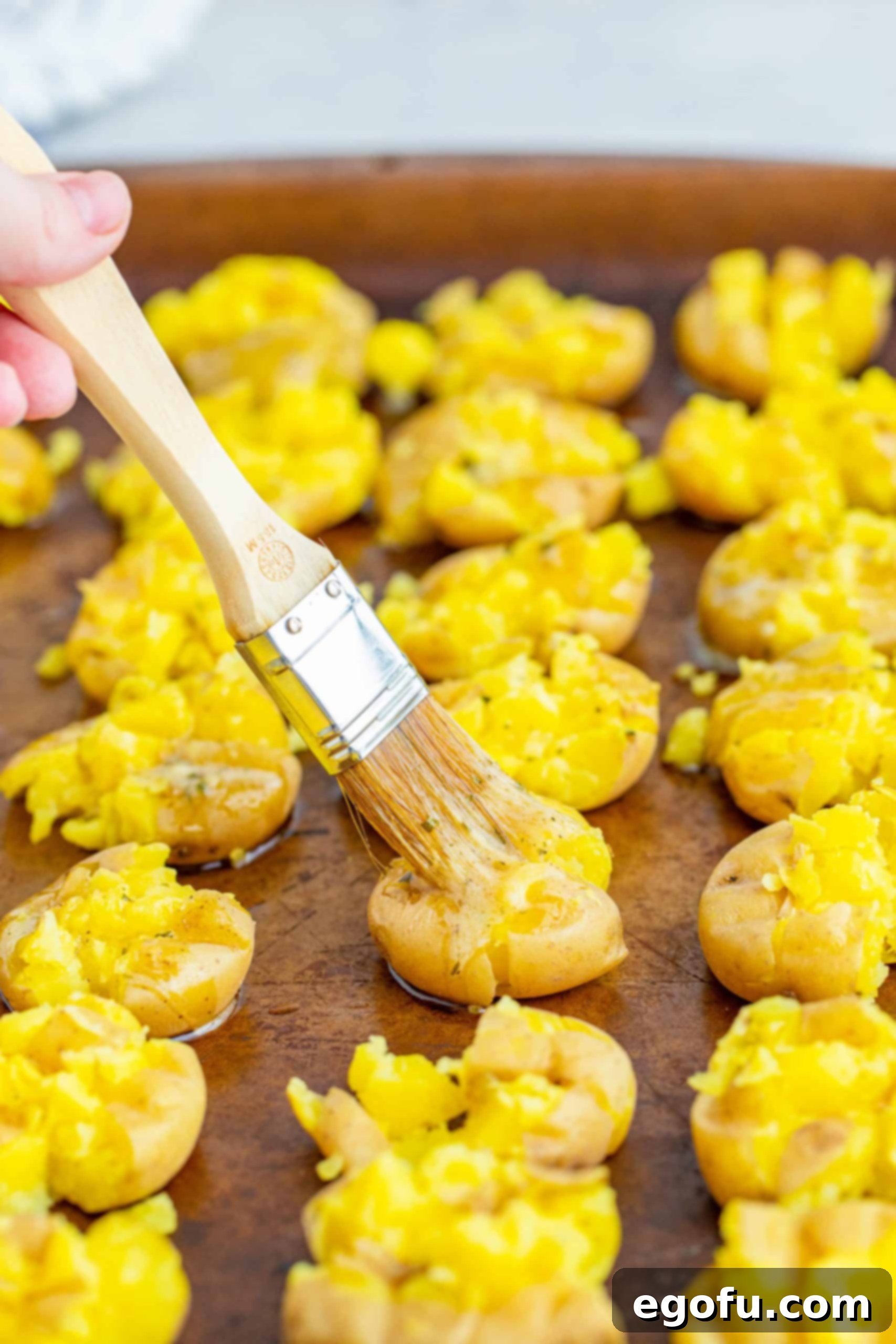 Pastry brush brushing butter ranch on smashed potatoes.