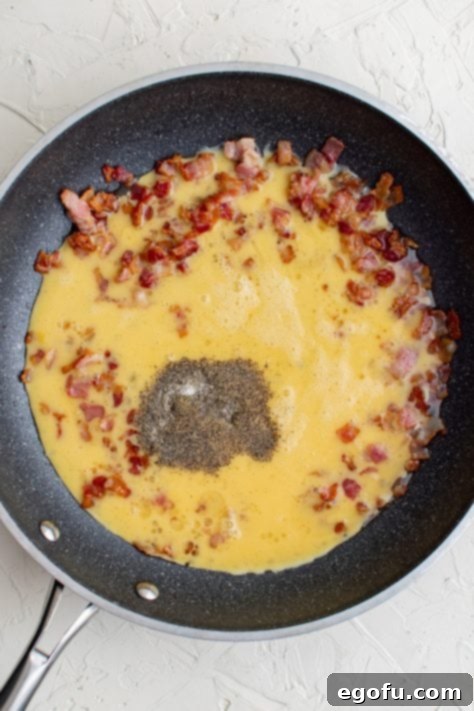 Eggs added to cooked bacon in pan