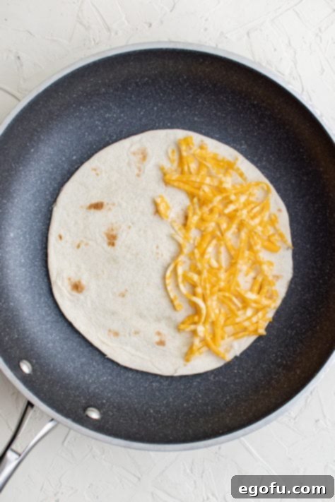 Tortilla added to pan topped with cheese on one side