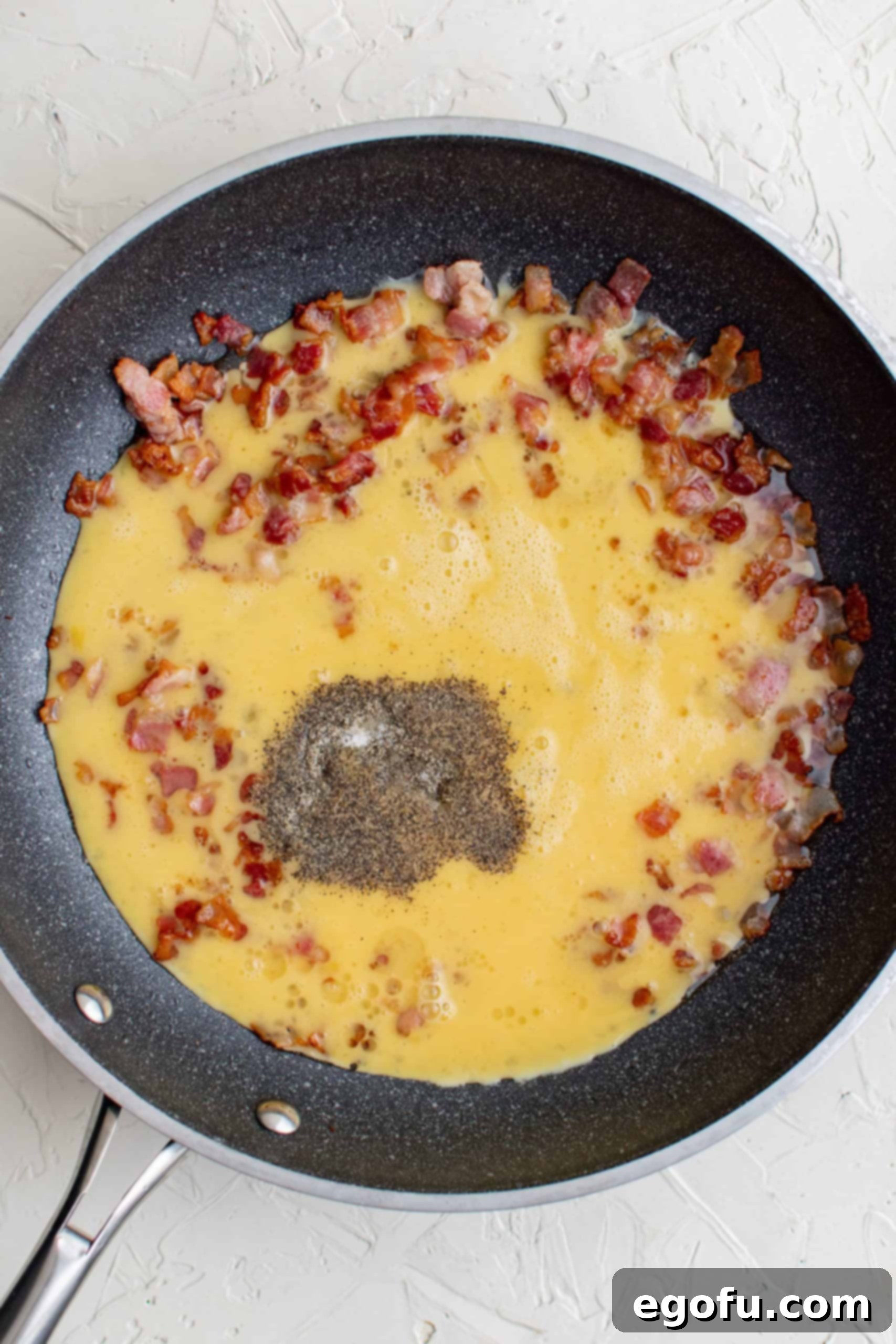 Eggs added to cooked bacon in pan.
