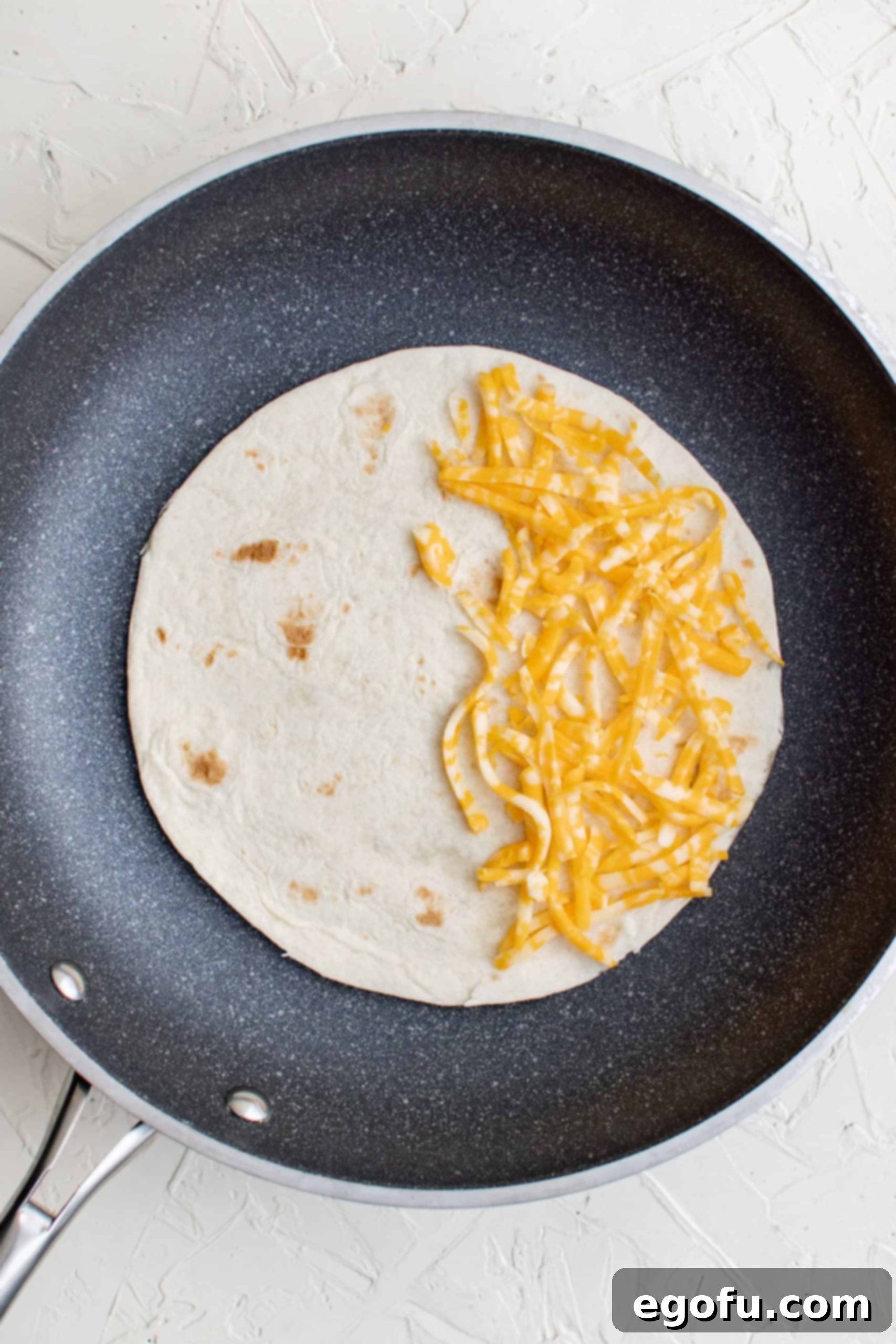 Tortilla added to pan topped with cheese on one side.