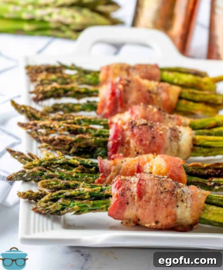 Crispy Air Fryer Bacon Asparagus Bundles 2 Air Fryer Bacon Wrapped asparagus lined up on a white serving tray.