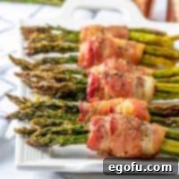 Crispy Air Fryer Bacon Asparagus Bundles 11 Air Fryer Bacon Wrapped asparagus lined up on a white serving tray.