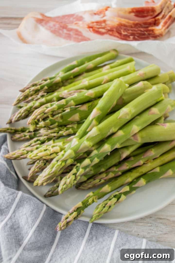 Crispy Air Fryer Bacon Asparagus Bundles 5 Snapped asparagus pieces on plate with thick cut bacon in the background.