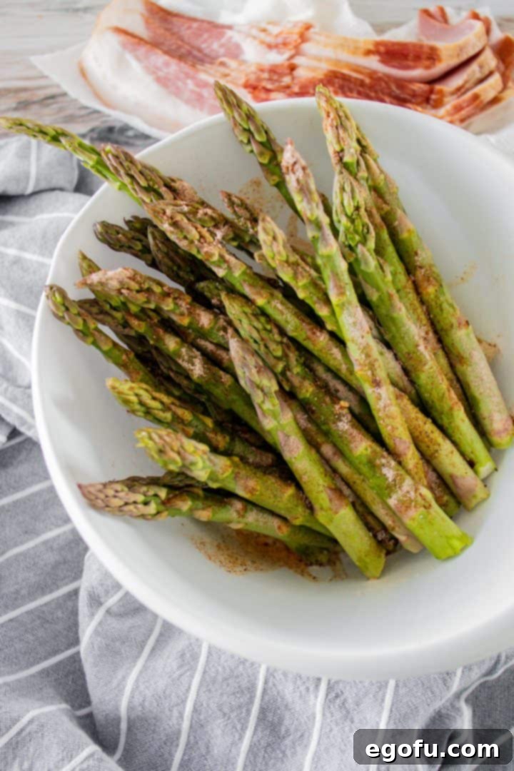Crispy Air Fryer Bacon Asparagus Bundles 6 Asparagus coated in seasonings and placed in a white bowl