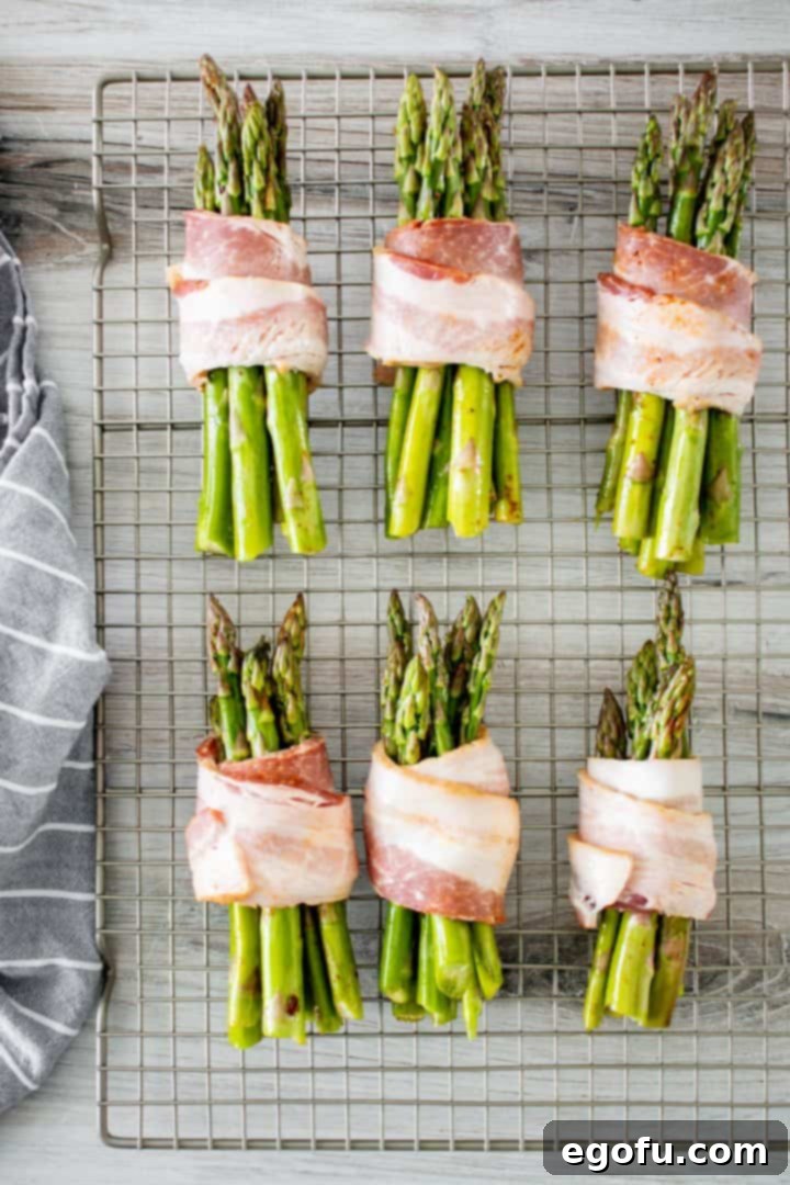 Crispy Air Fryer Bacon Asparagus Bundles 7 Bundles of asparagus wrapped in bacon on wire rack.