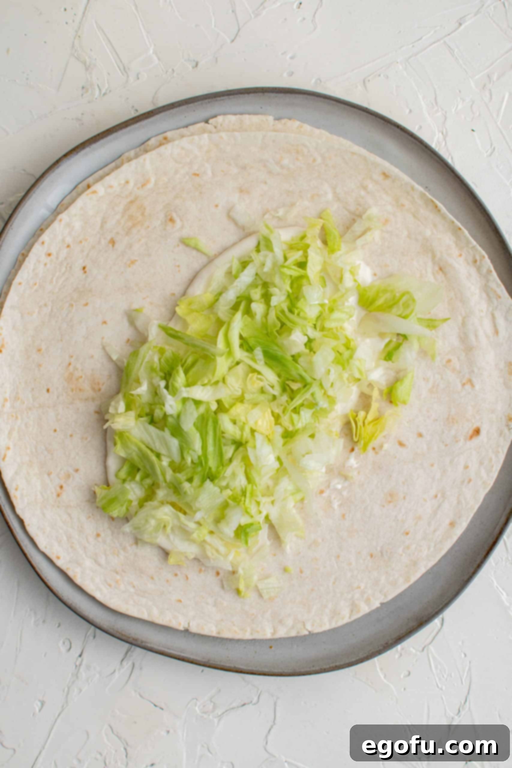Shredded lettuce on top of sauce on tortilla.