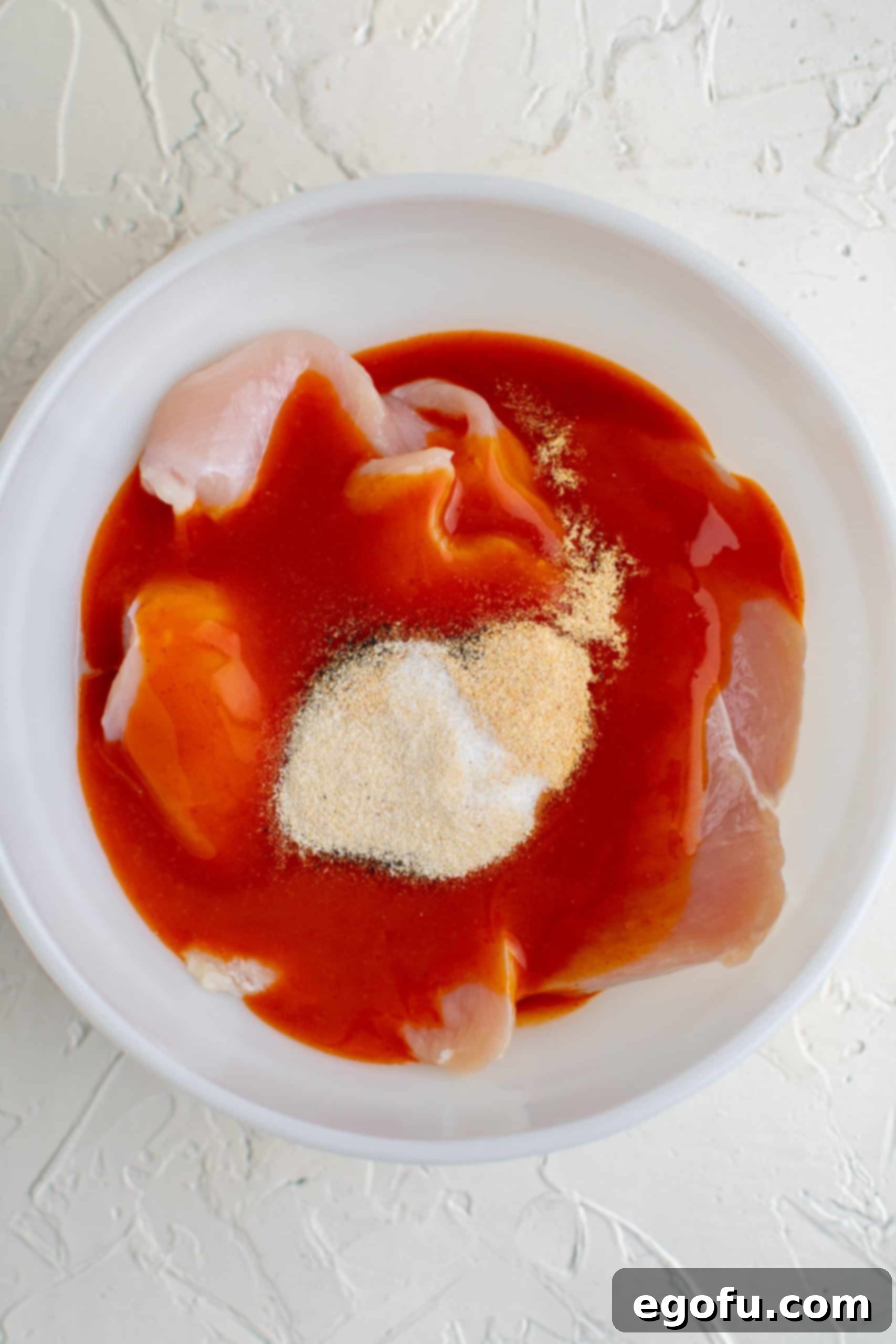 Chicken in bowl covered in hot sauce, and spices.