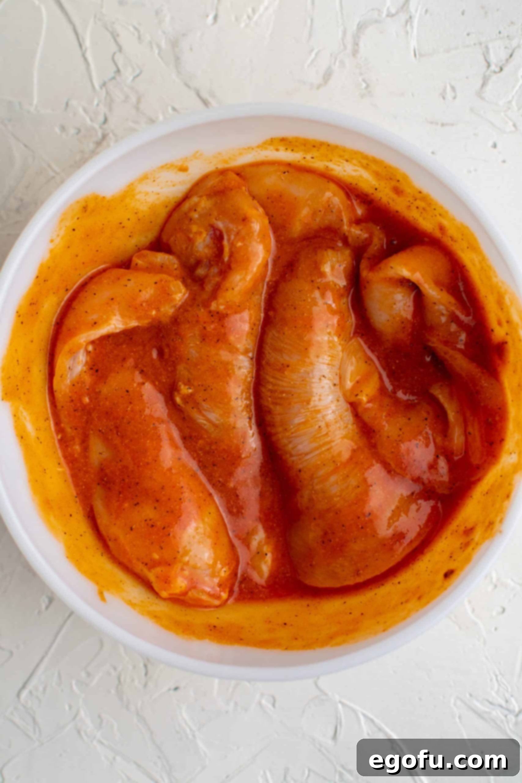 Chicken mixed up with buffalo and spices in bowl.