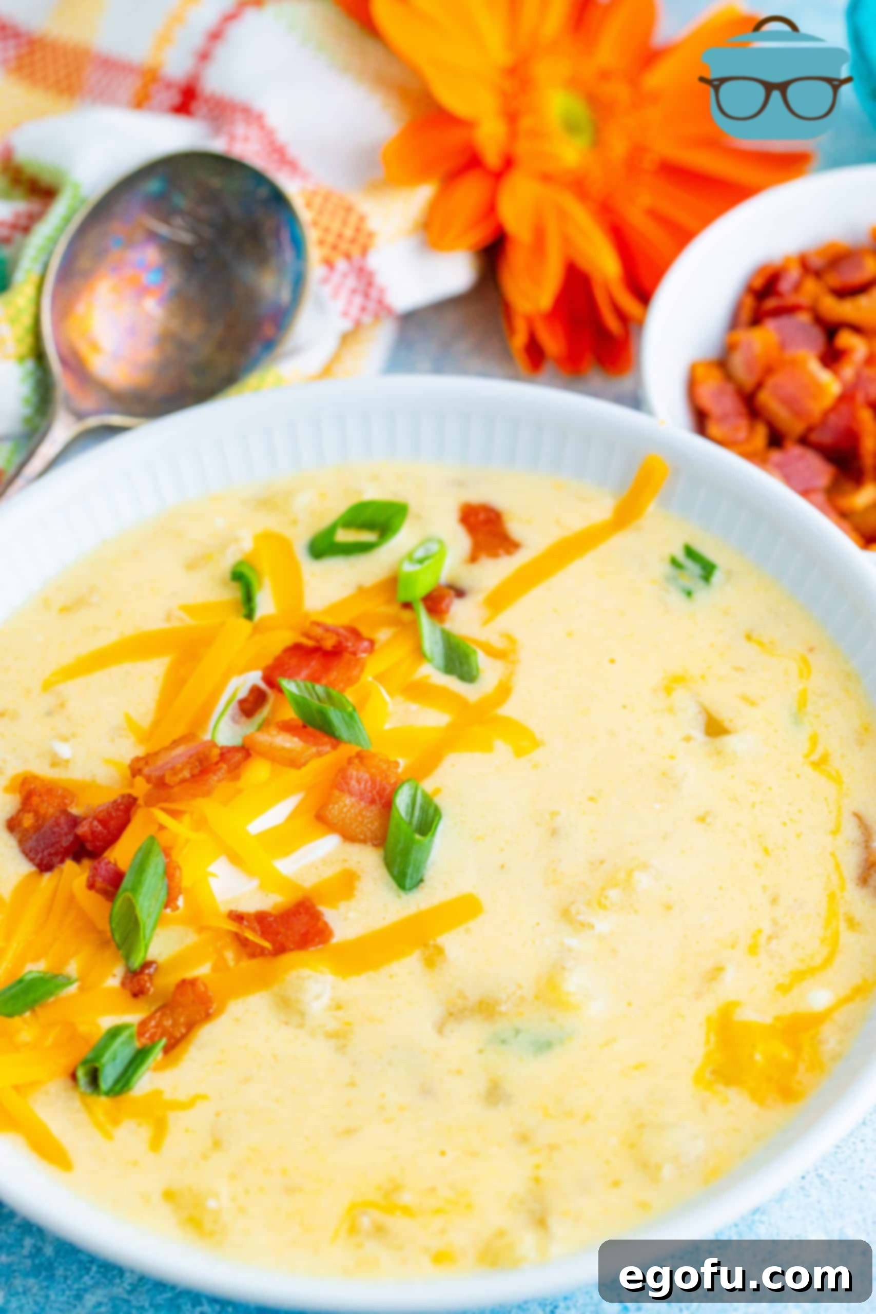 A serving of Instant Pot Loaded Potato Soup in a white bowl, generously topped with bacon, green onions, and shredded cheese.