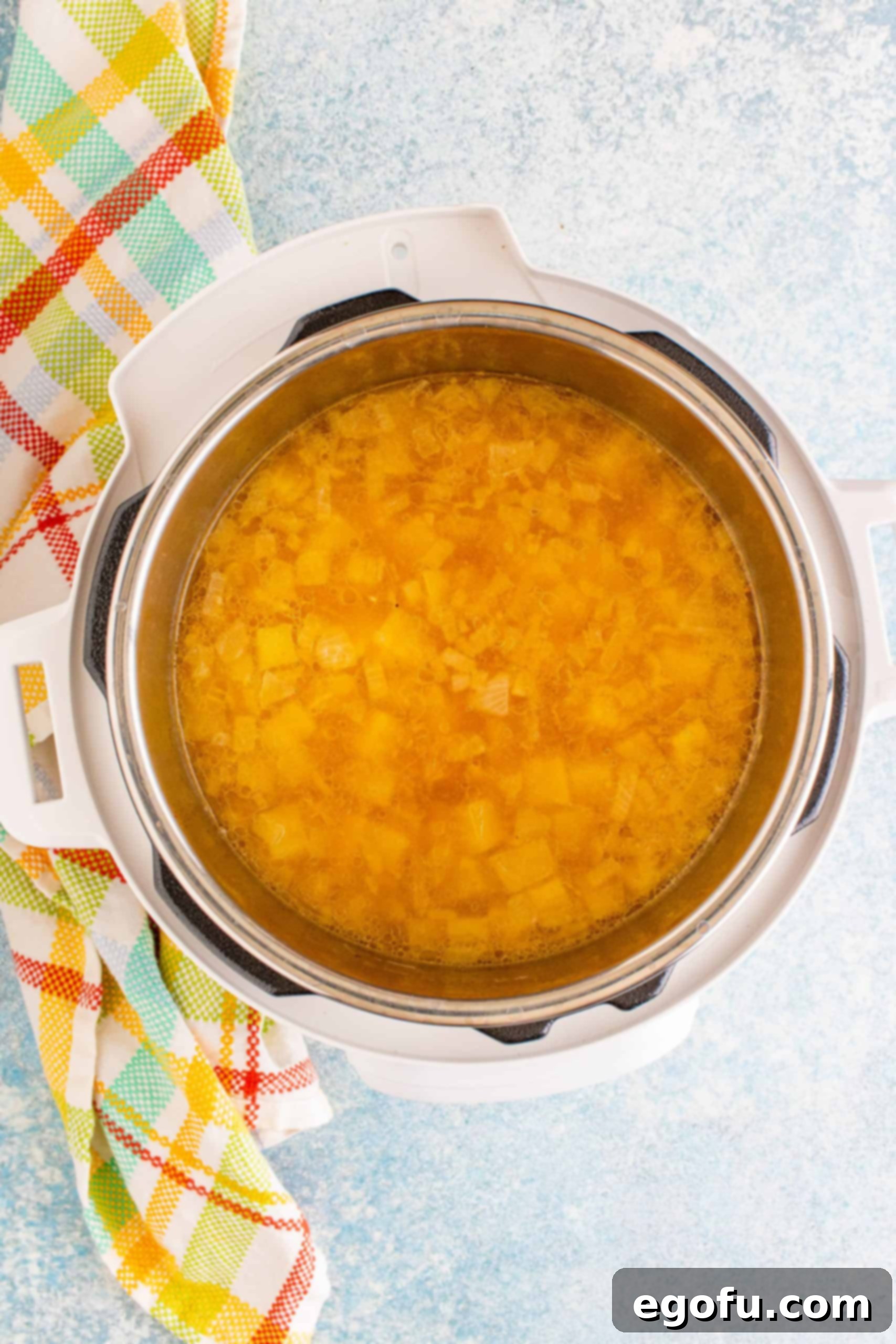 Cooked potatoes in chicken broth within the Instant Pot, being mashed with a potato masher.