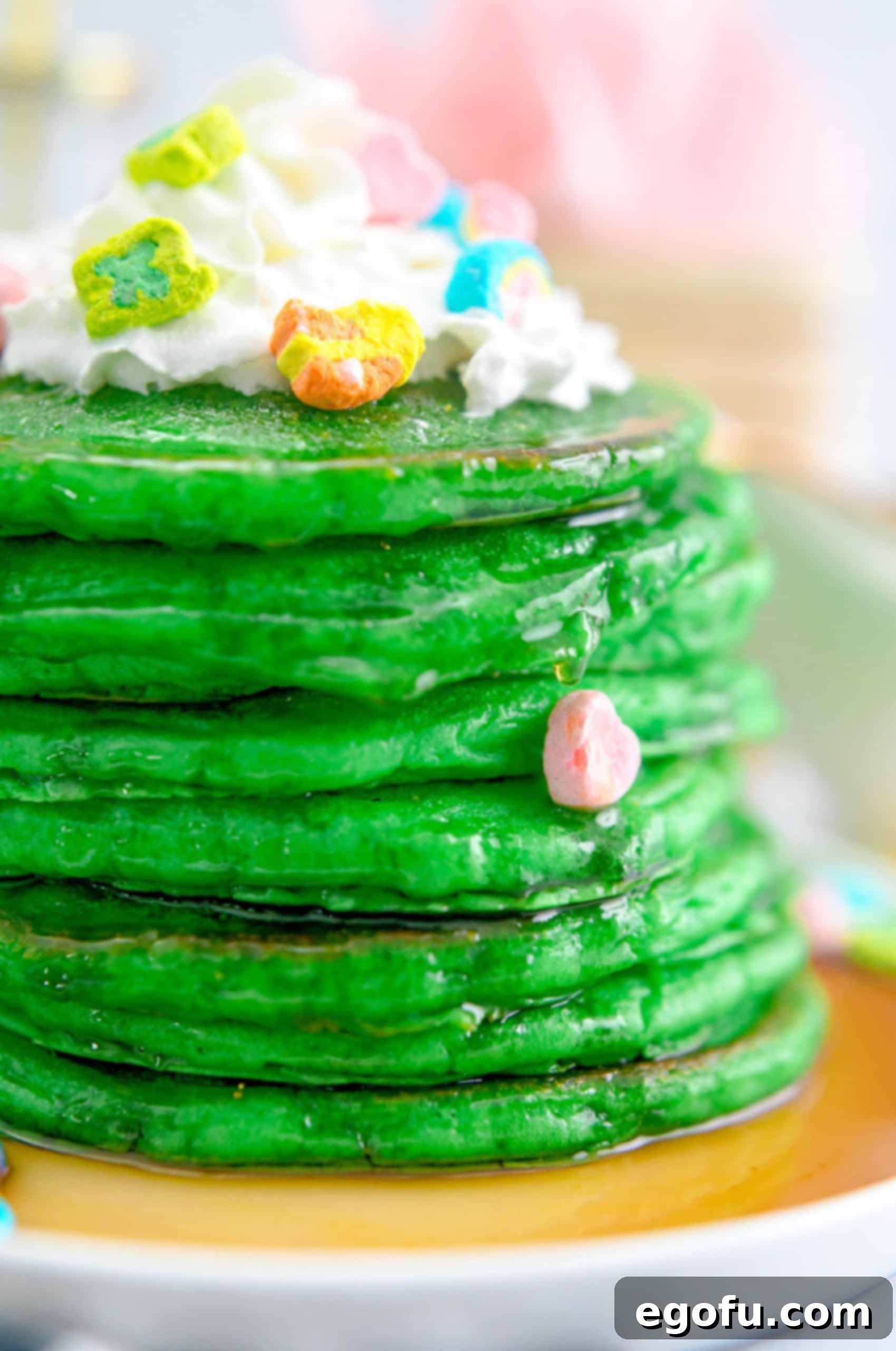 Stack of vibrant green St. Patrick's Day Pancakes with golden syrup, fluffy whipped cream, and festive marshmallows for a fun holiday breakfast.