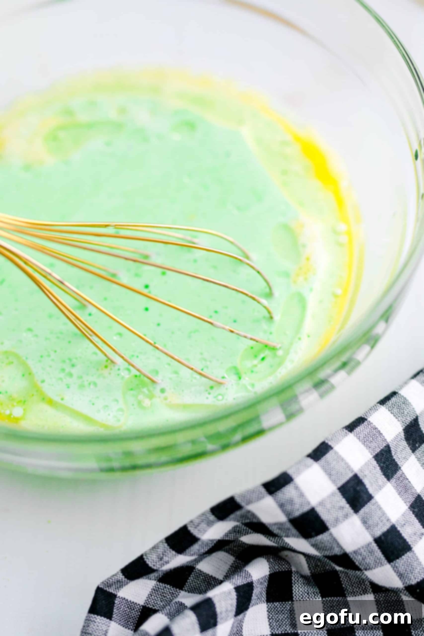 A whisk gently combining the green wet ingredients with the dry ingredients in a bowl, forming a perfectly lumpy pancake batter.