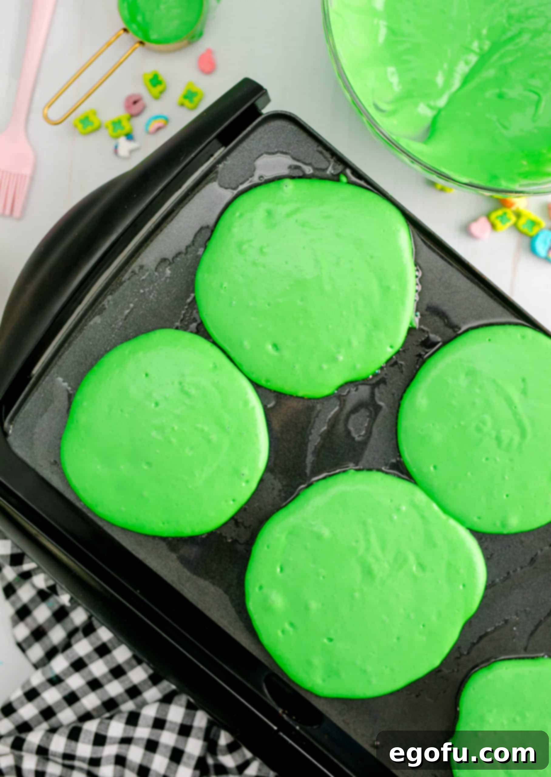 Several green pancakes cooking on a griddle, with some beginning to bubble and dry at the edges, indicating they are ready to be flipped.