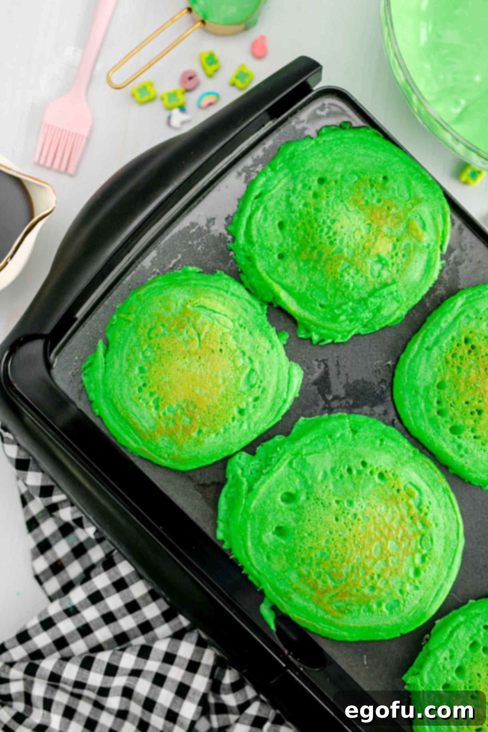 Freshly cooked St. Patrick's Green Pancakes resting on a griddle, displaying their vibrant color and fluffy texture, ready to be served.