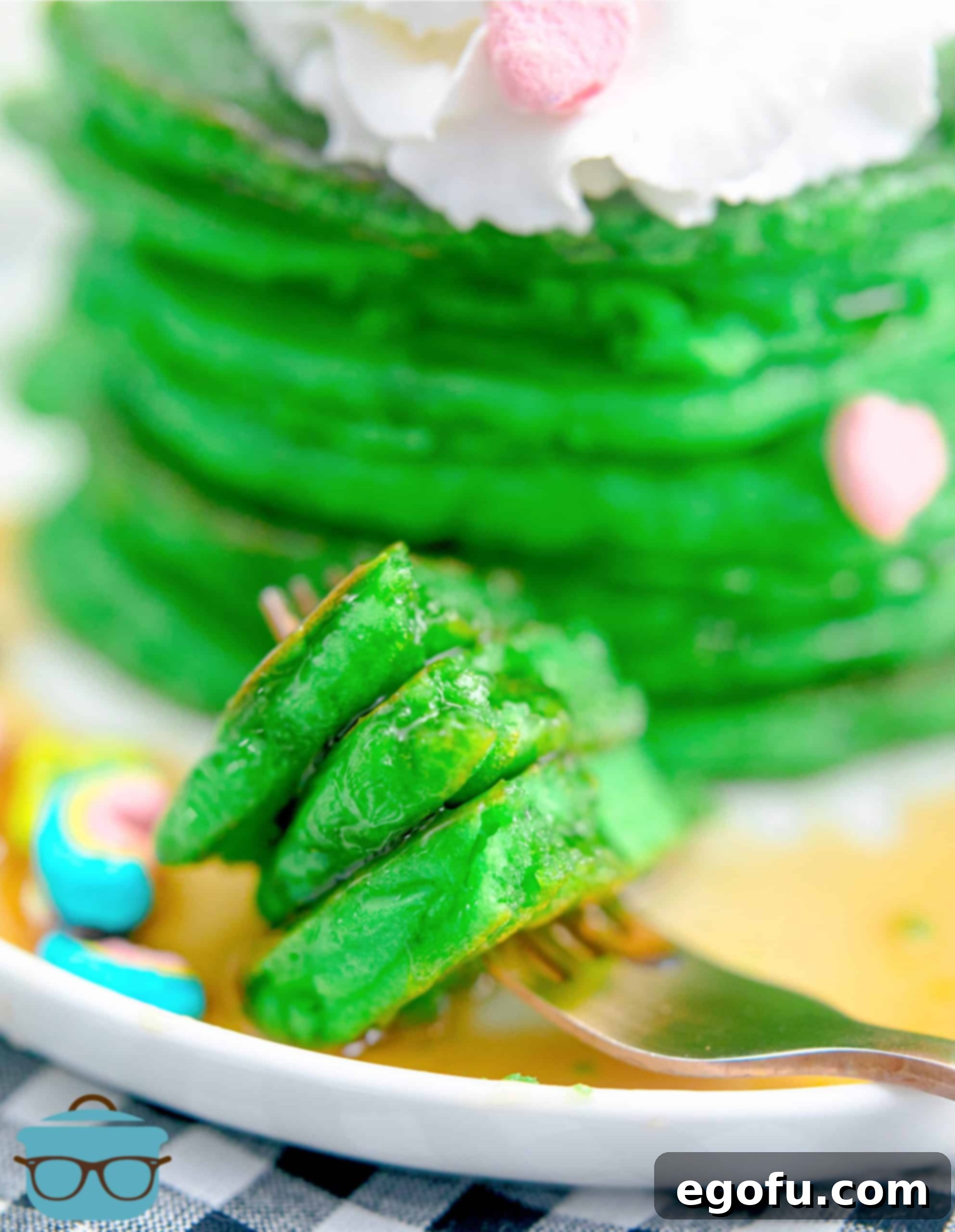 A fork taking a bite out of a stack of St. Patrick's Green Pancakes, revealing the fluffy interior and delightful toppings, perfect for a festive breakfast.