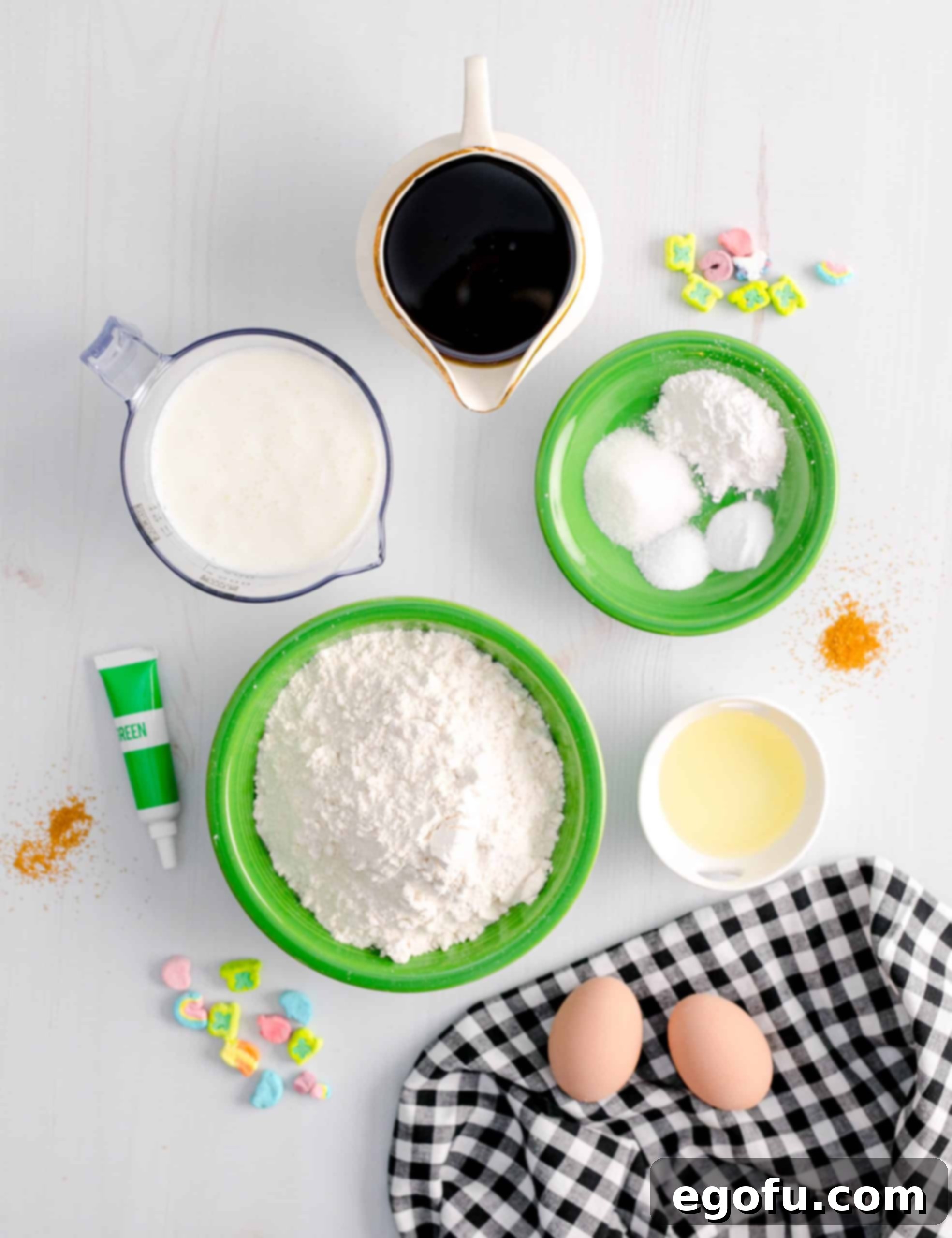 A collection of ingredients laid out, ready to be used for making St. Patrick's Green Pancakes, including flour, sugar, eggs, and food coloring on a wooden surface.