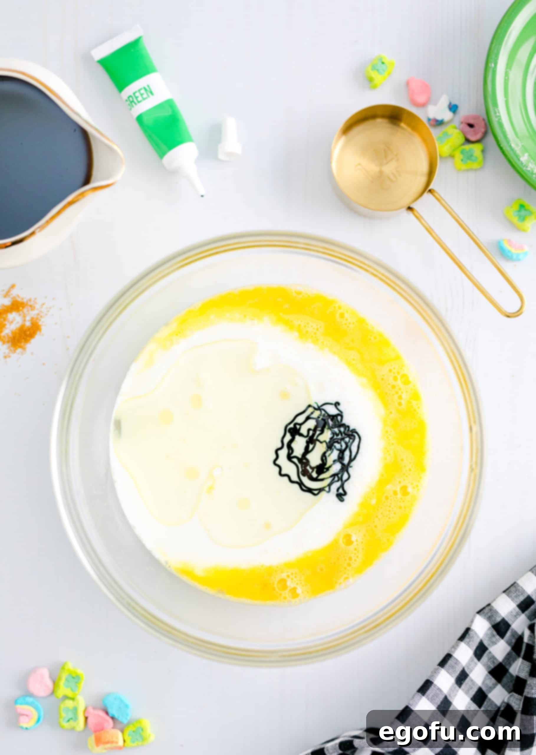A bowl containing the wet ingredients for pancakes, including beaten egg, oil, buttermilk, and green food coloring, all mixed together into a vibrant hue.