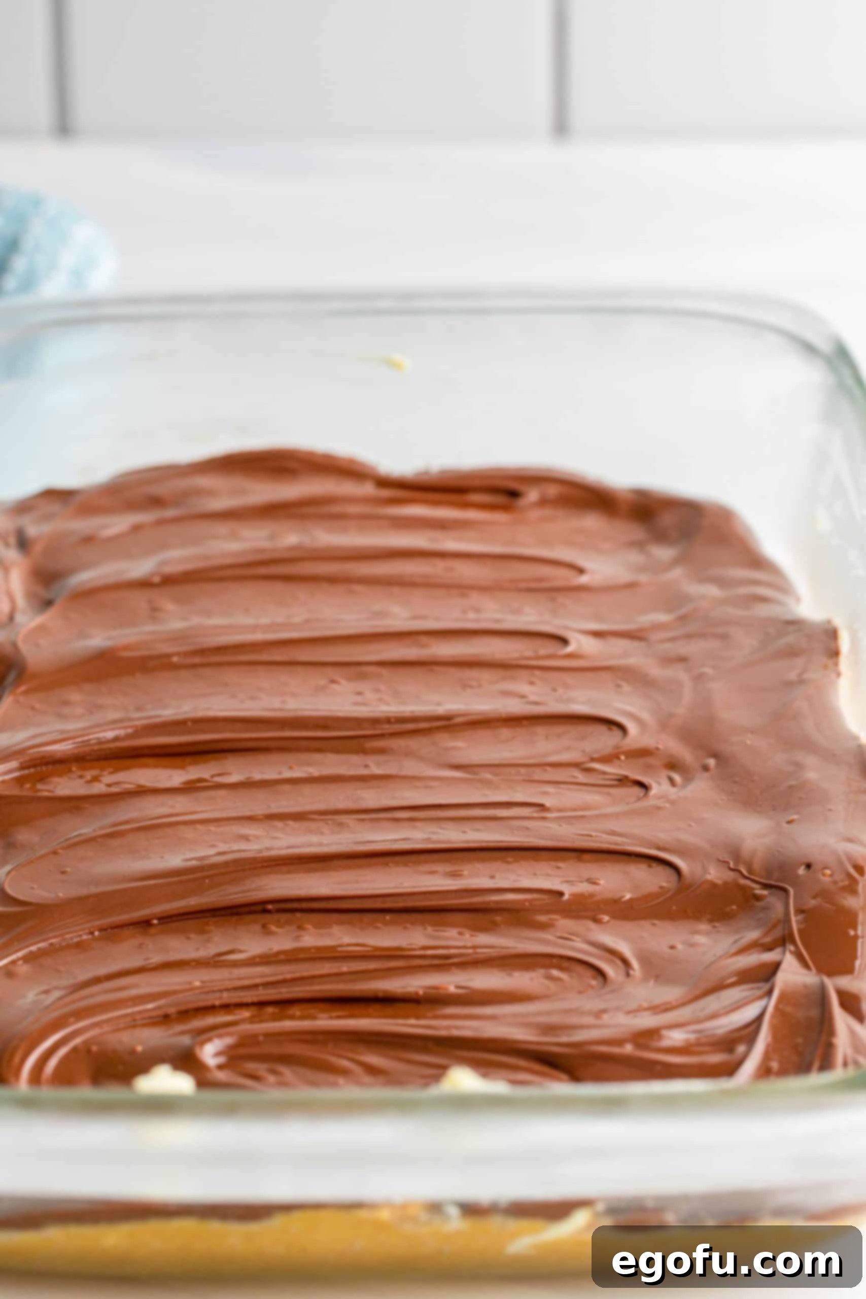 Grandma's No-Bake Peanut Butter Dream Bars 12 The baking dish with a perfectly spread layer of melted chocolate over the peanut butter mixture, chilling in the freezer.